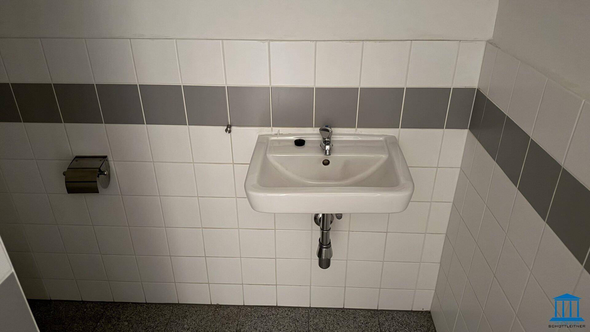 Einfaches Waschbecken in einer Gästetoilette mit weißen und grauen Fliesen, funktional und sauber.