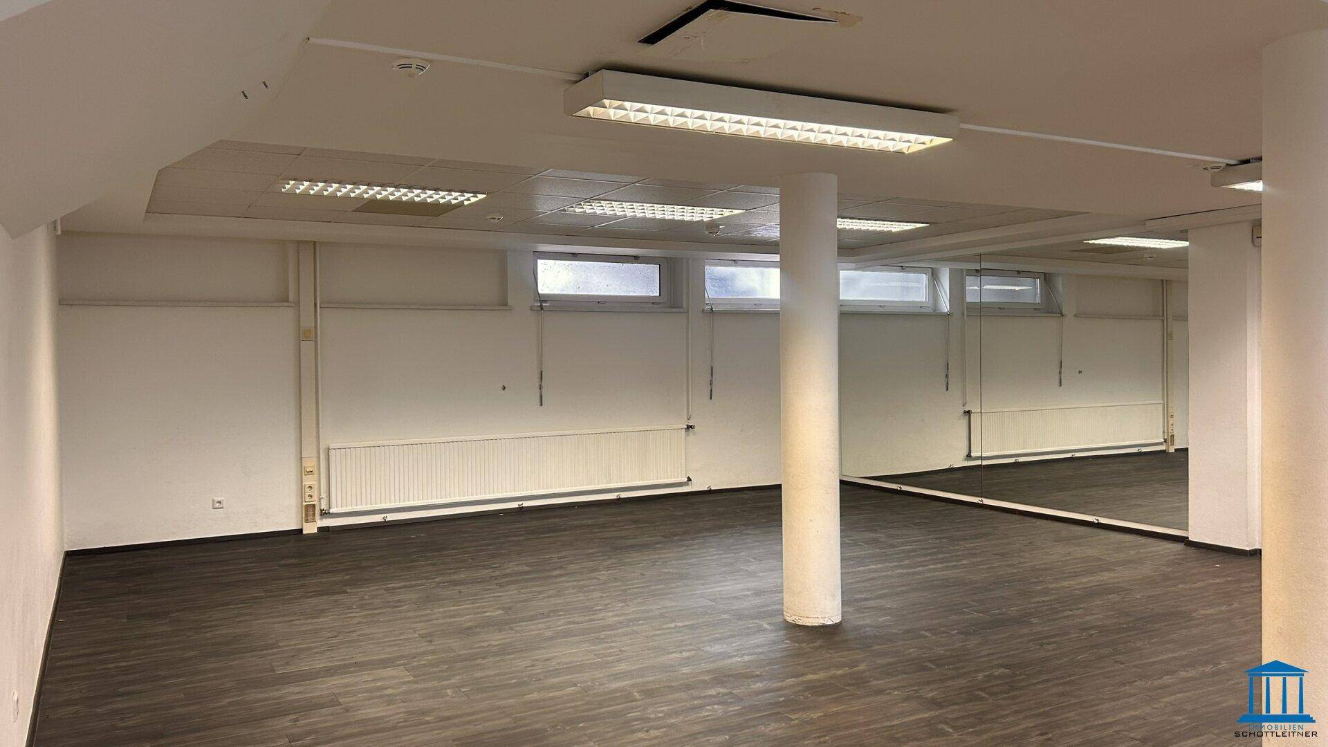 Großer, leerer Büroraum mit dunklem Laminatboden, Säule und hohen Fenstern.