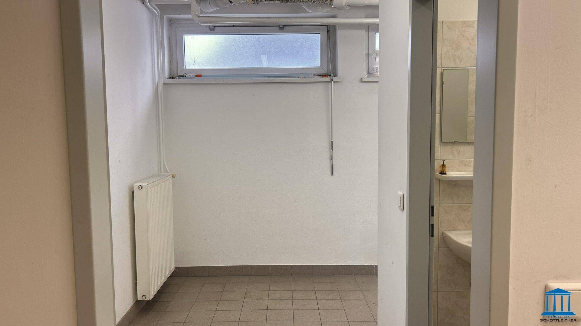 Kleiner Abstellraum mit Fenster, Heizkörper und gefliestem Boden, angrenzend an ein Badezimmer.