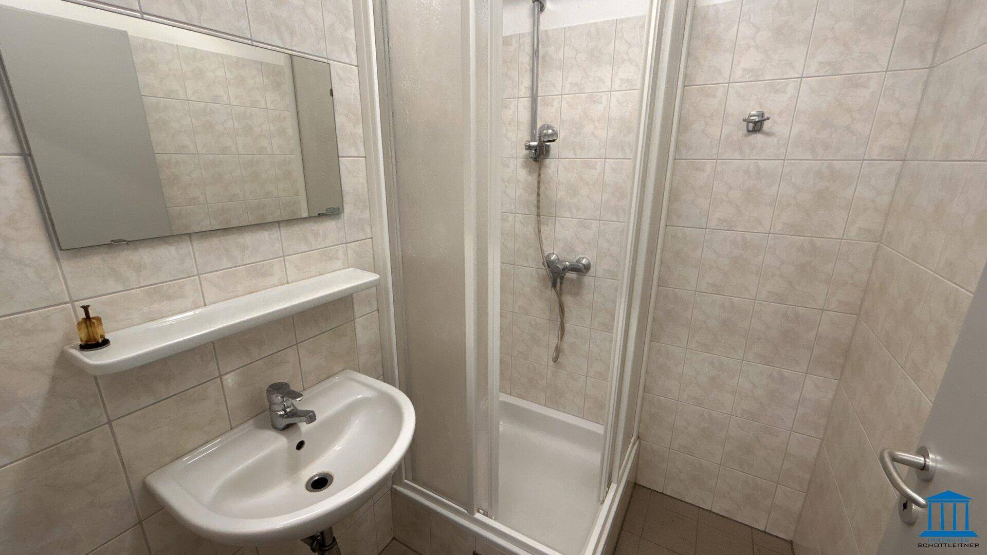 Funktionales Badezimmer mit Duschkabine, Waschbecken und Spiegel, komplett gefliest.