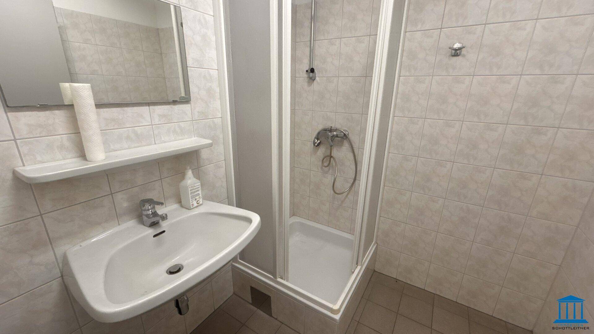 Funktionales Badezimmer mit Duschkabine, Waschbecken und Spiegel, komplett gefliest.