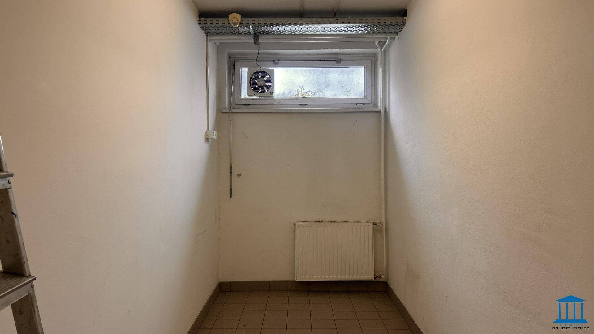 Kleiner Raum mit Fenster, Abluftventilator, Heizkörper und gefliestem Boden.