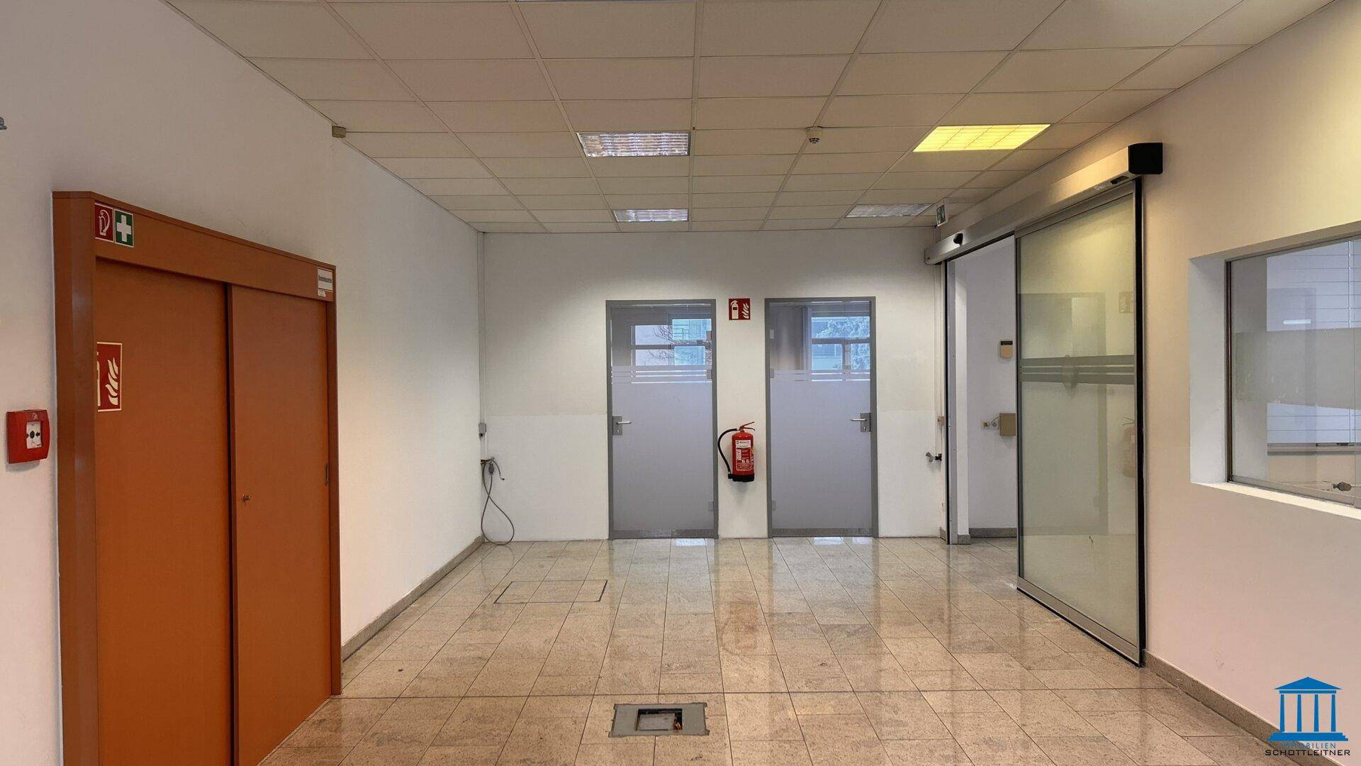 Flurbereich mit gefliestem Boden, Aufzugstür und weiteren Türen zu Büros.