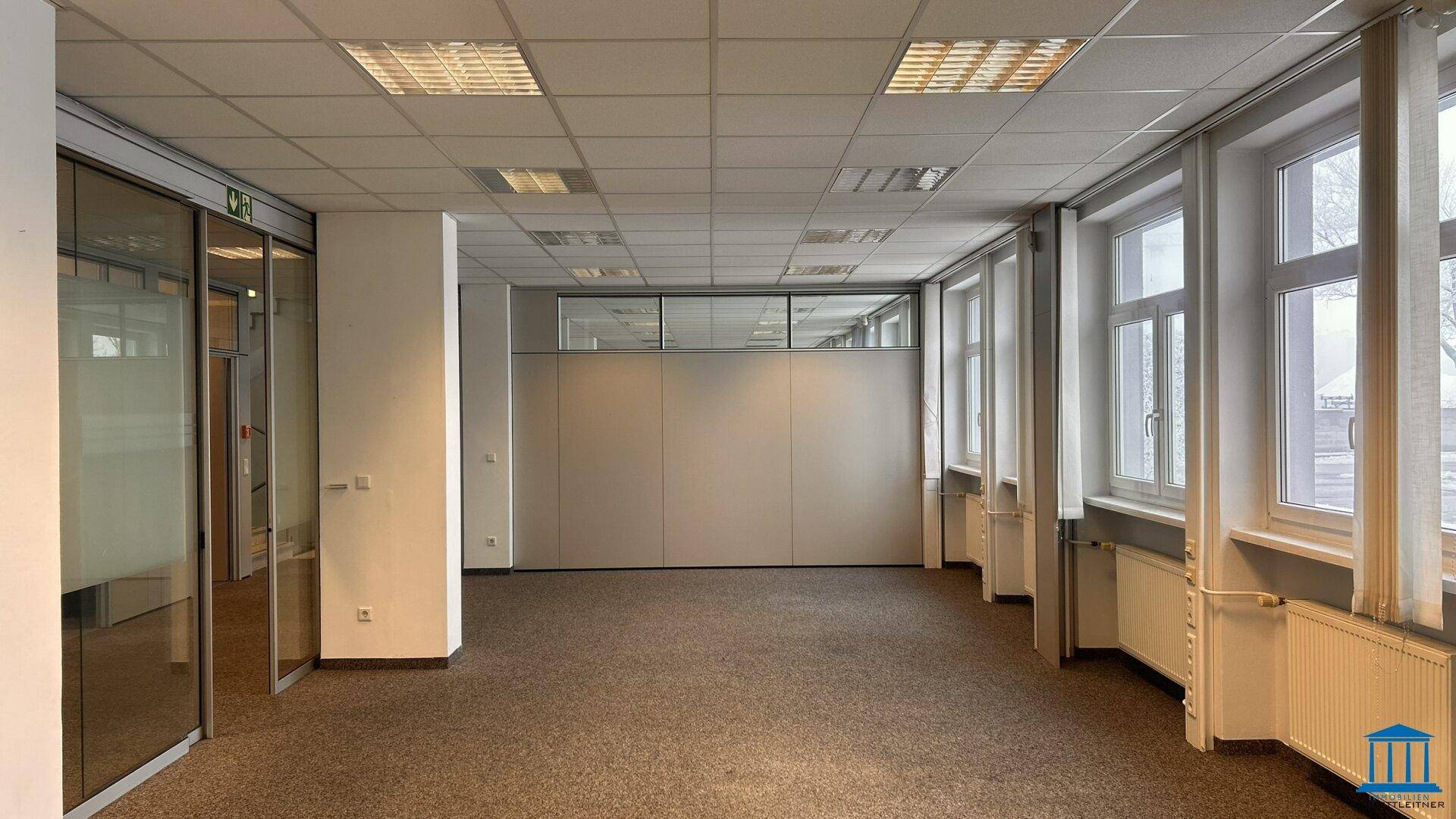 Großer Büroraum mit Teppichboden, vielen Fenstern mit Jalousien und Glasabtrennungen.