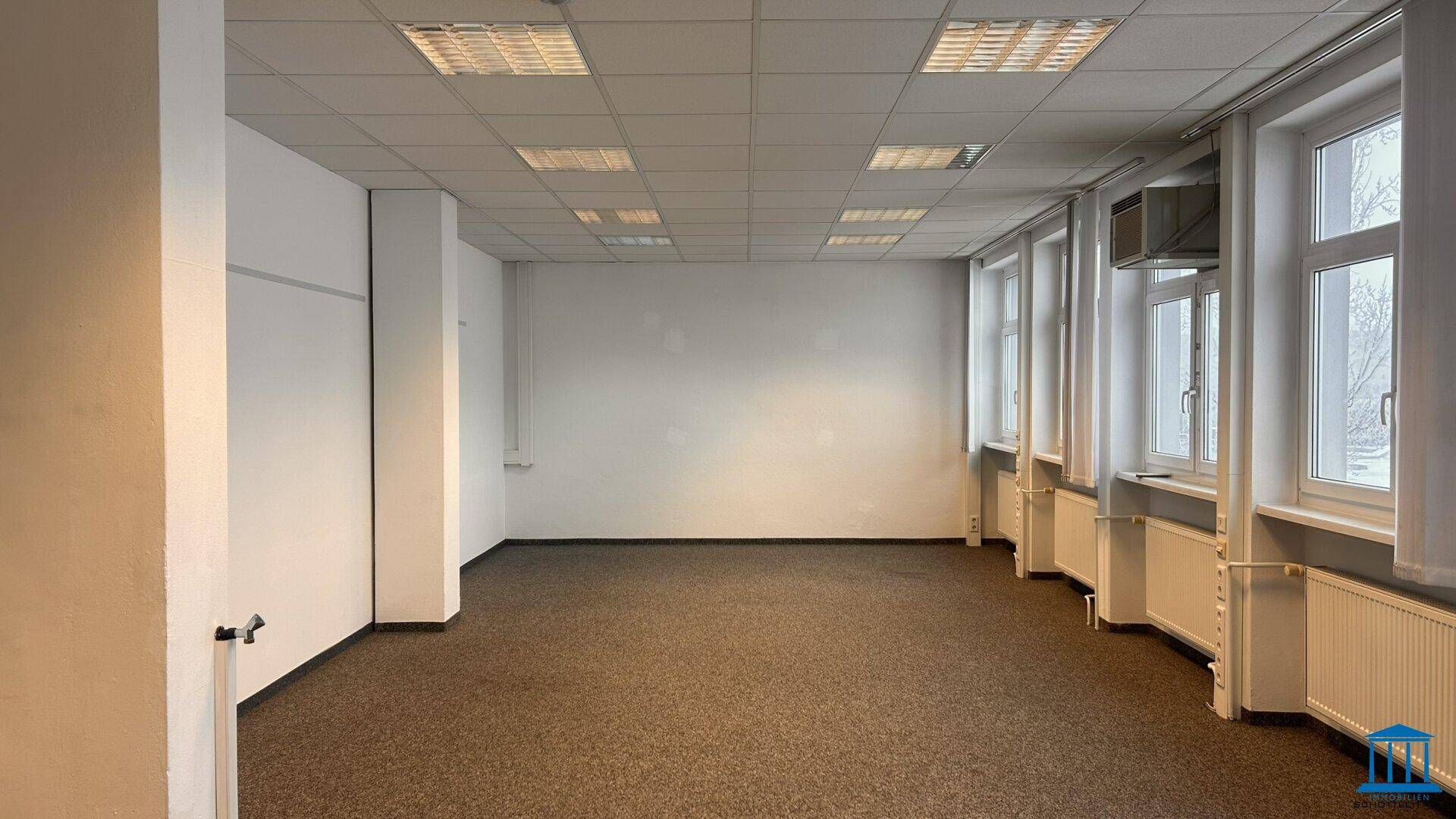 Leeres Büro mit Teppichboden, Klimaanlage, Fenstern und weißen Wänden, bietet eine komfortable Arbeitsumgebung.