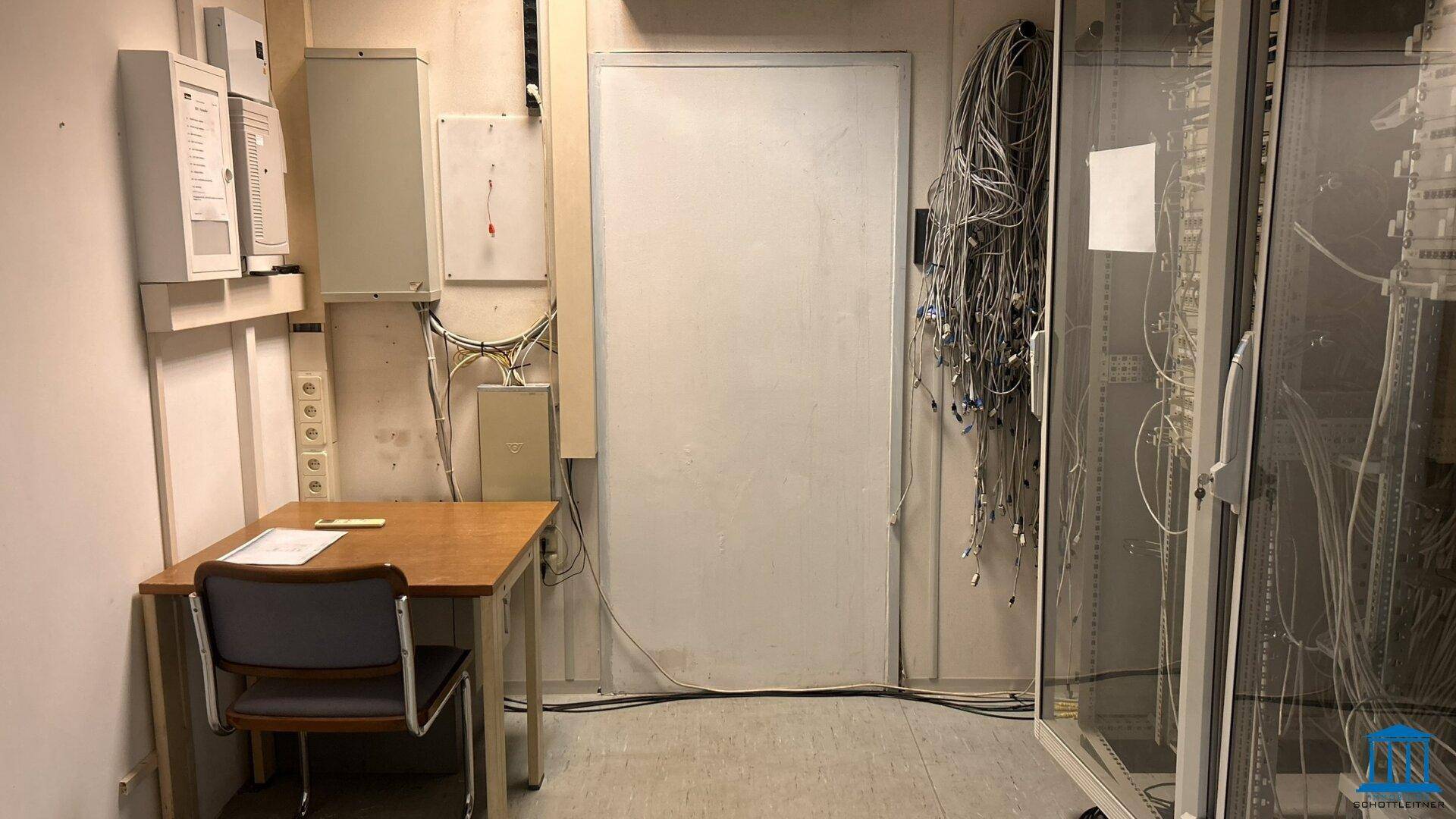 Technikraum mit zahlreichen Kabeln, einem Schreibtisch und Server-Equipment, essenziell für die Infrastruktur.