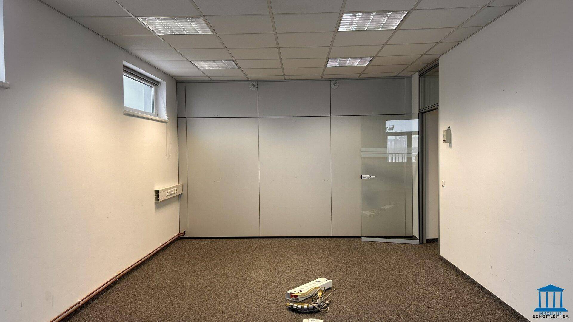 Modernes Bürozimmer mit Teppichboden, Trennwand und Glastür, die den Raum offen und hell wirken lässt.