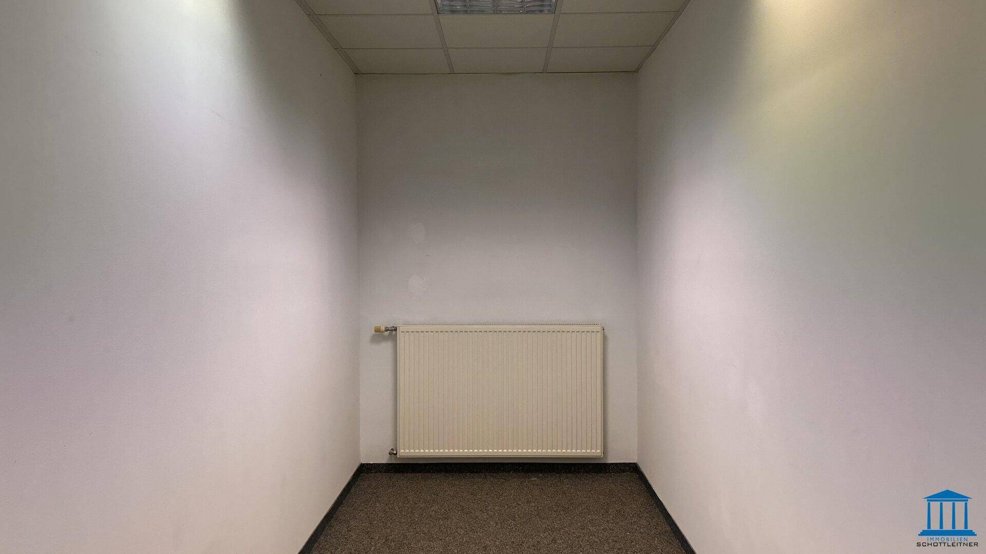 Kleiner, leerer Raum mit Teppichboden und Heizkörper, ideal als Abstellraum nutzbar.