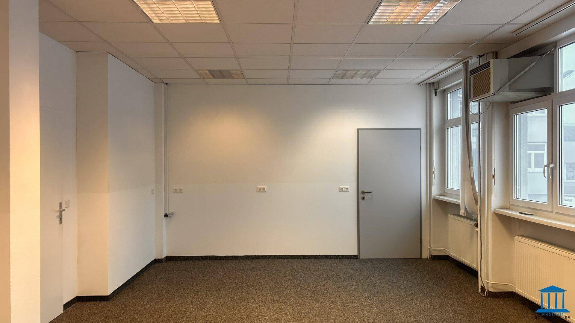 Helles Büro mit Teppichboden, einer Tür und einem Fenster mit Klimaanlage.
