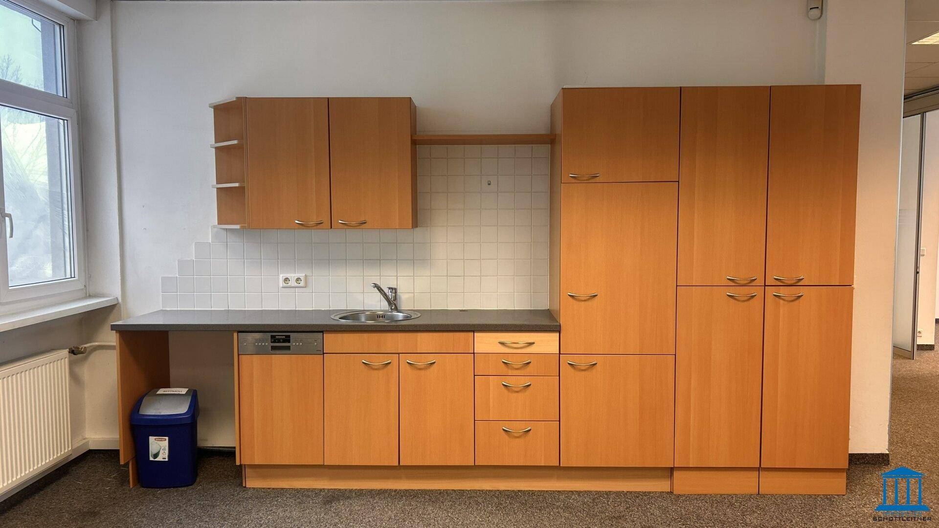Funktionale Einbauküche mit Holzschränken, Spülmaschine und Fenster für natürliche Belüftung.