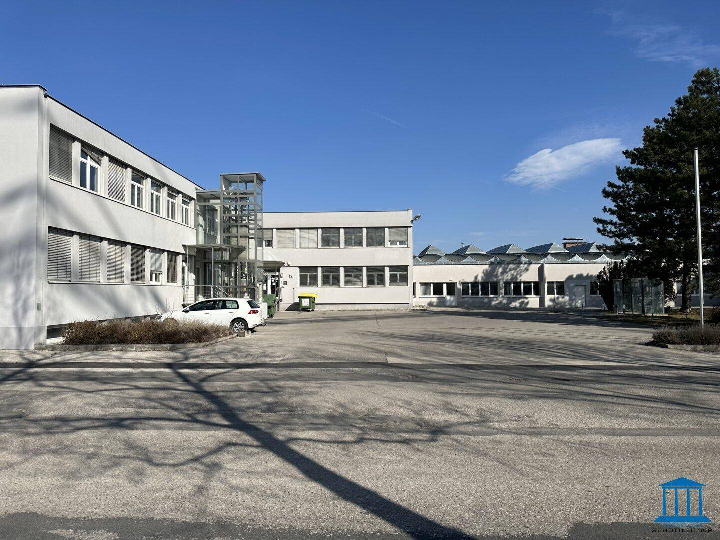 Weitläufiger Außenbereich eines Gewerbekomplexes mit Parkplätzen und mehreren Gebäuden unter klarem Himmel.