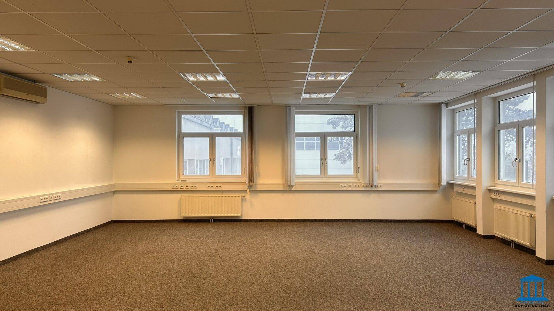 Geräumiges, leeres Büro mit Teppichboden, mehreren Fenstern und Klimaanlage.
