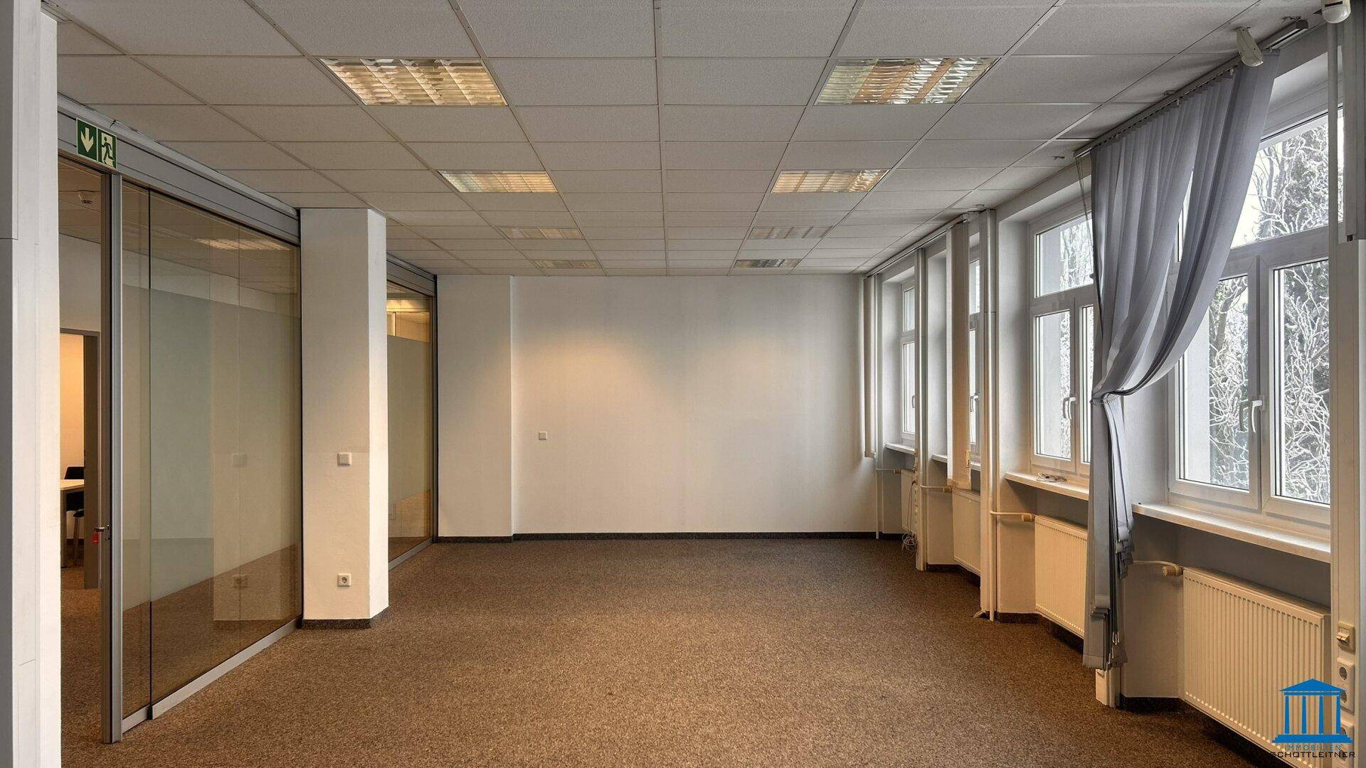 Büro mit Teppichboden, Fensterfront und Vorhängen, bereit zur Einrichtung.