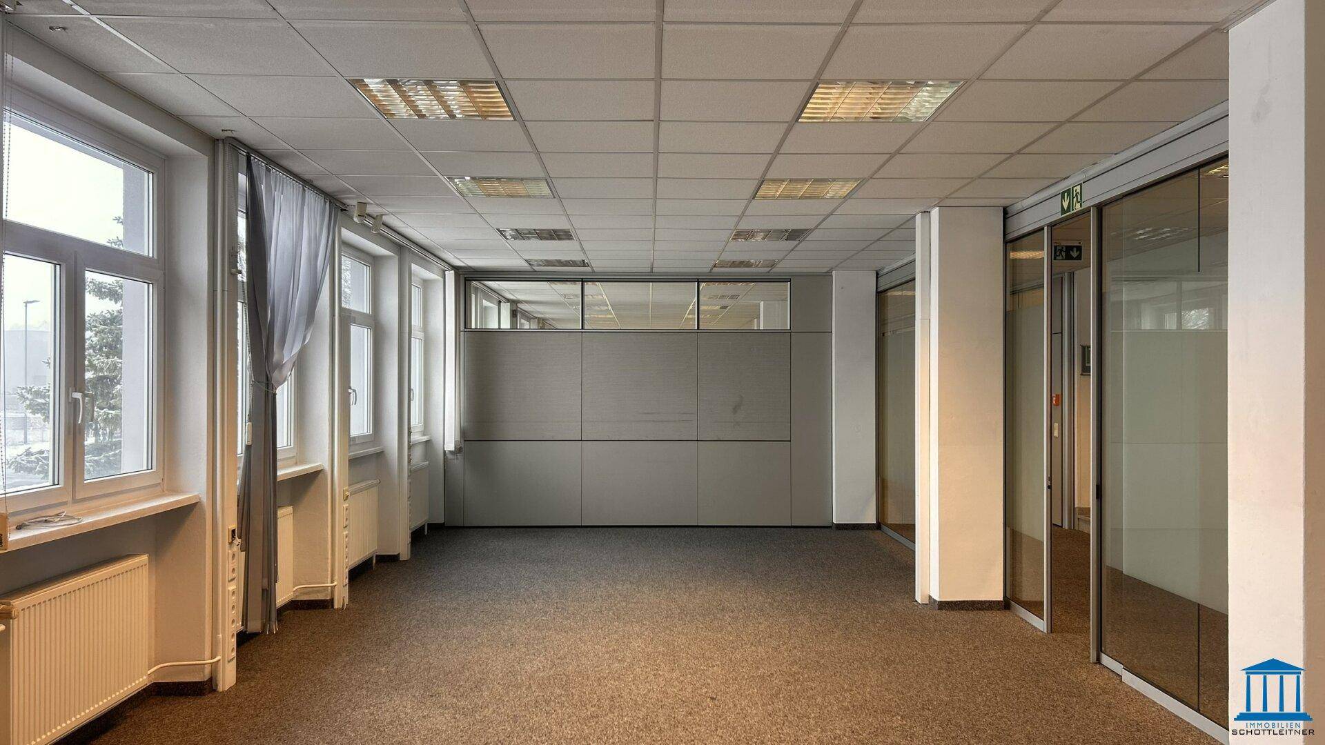 Geräumiges Büro mit Teppichboden, Fensterfront und modularen Trennwänden.