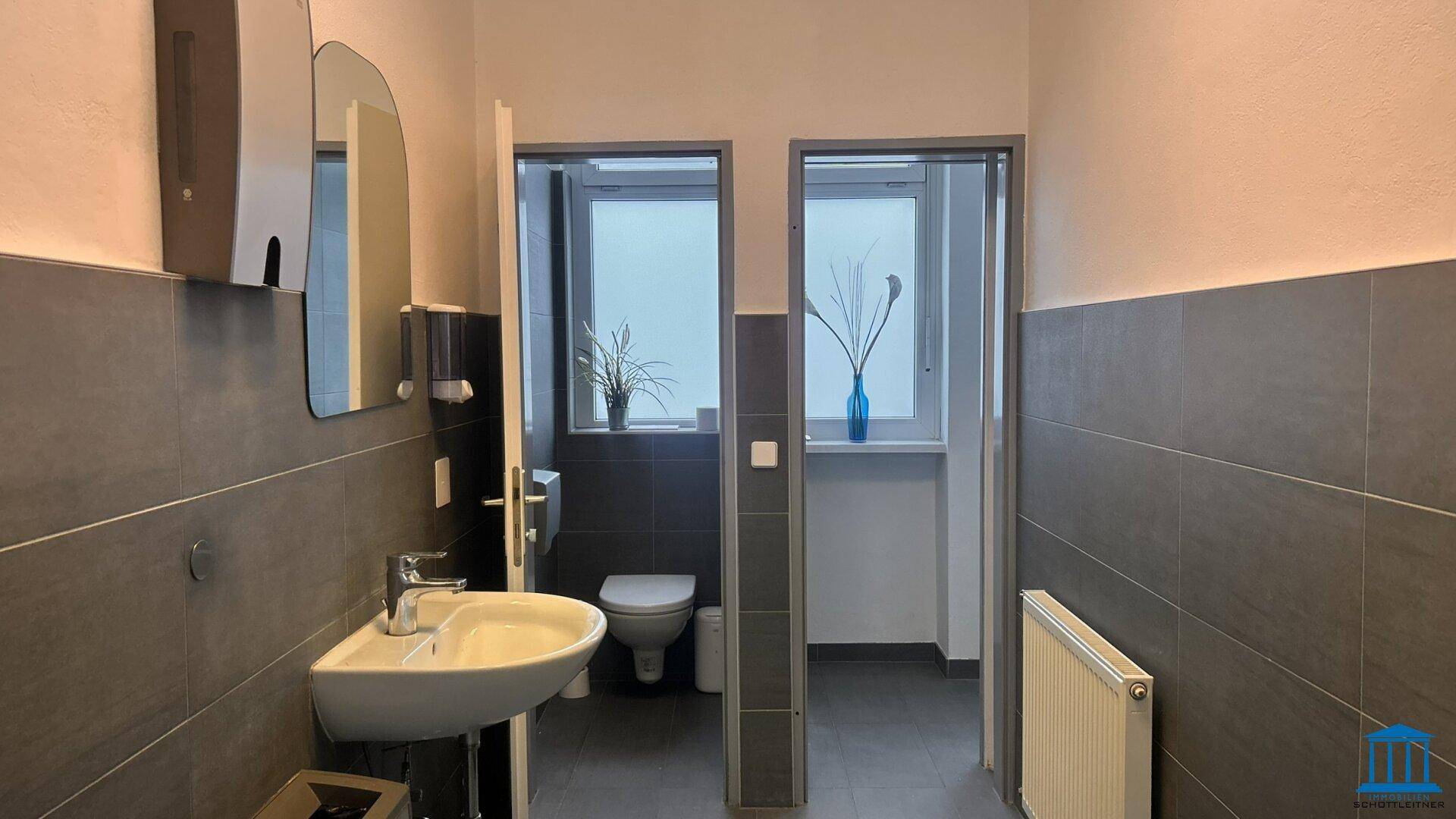 Modernes Badezimmer mit grauen Fliesen, Waschbecken und Toilette.