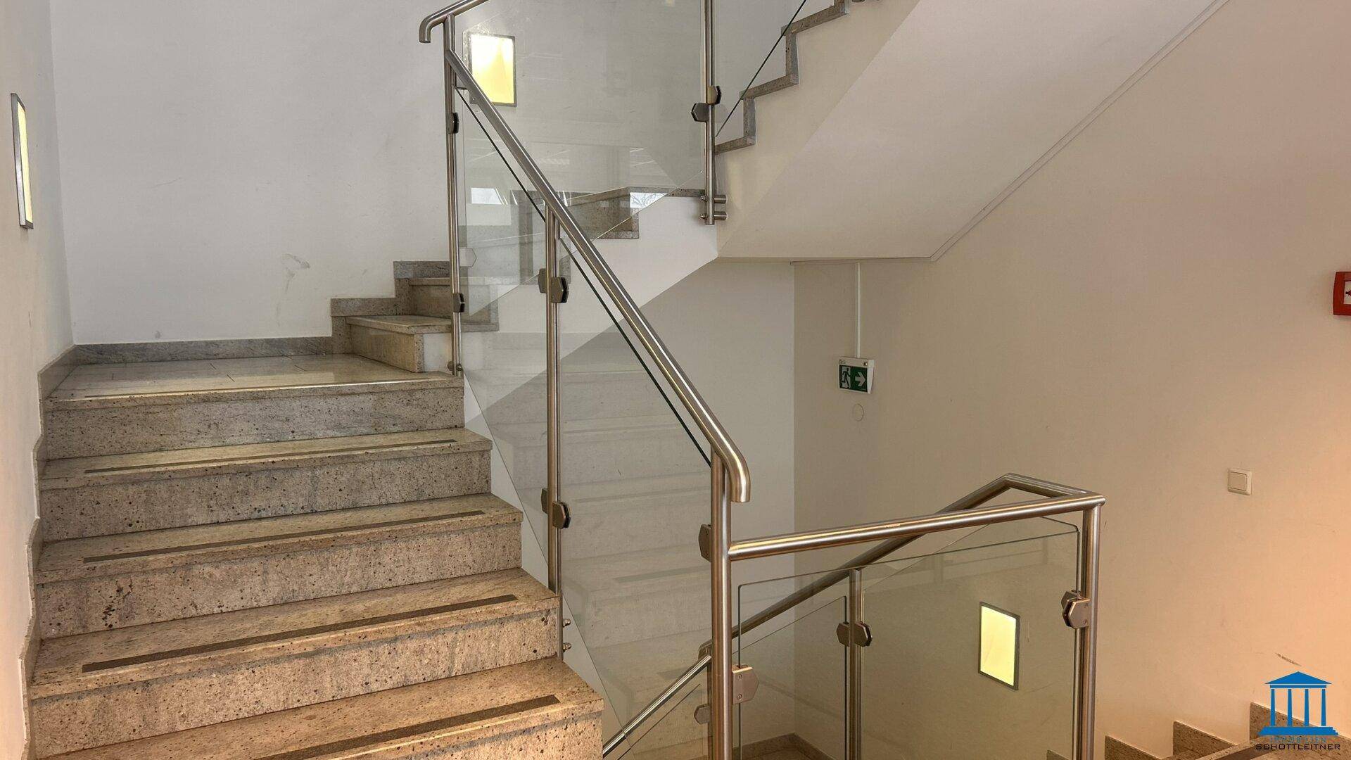 Treppenhaus mit Granitstufen und modernem Glasgeländer.