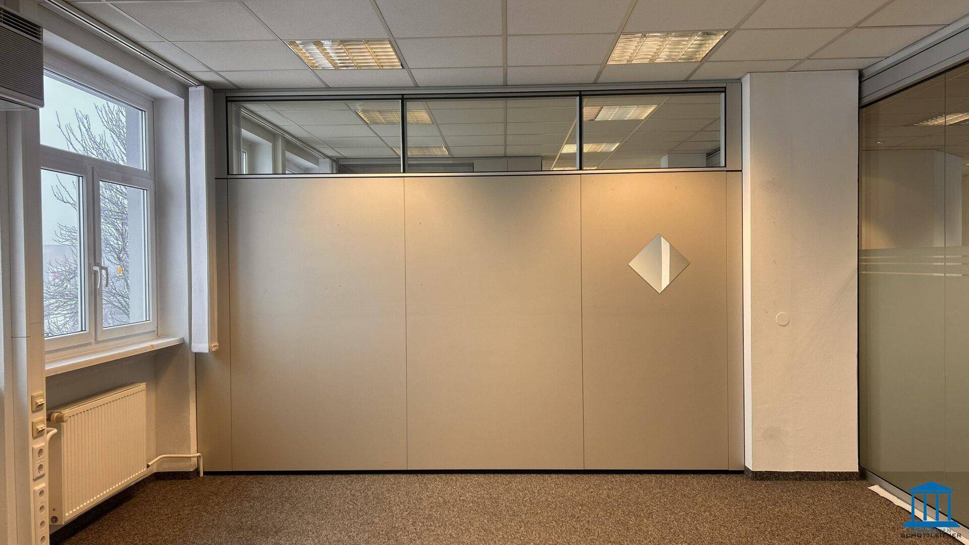 Leeres Büro mit Teppichboden, Fenster und modularen Trennwänden.