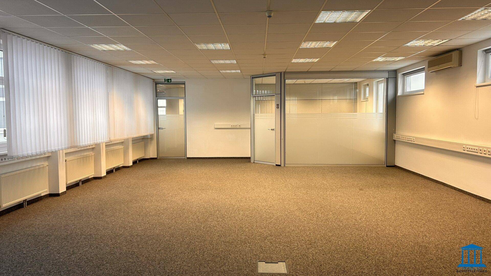 Geräumiges Büro mit Teppichboden, Fensterfront und Glaswänden.