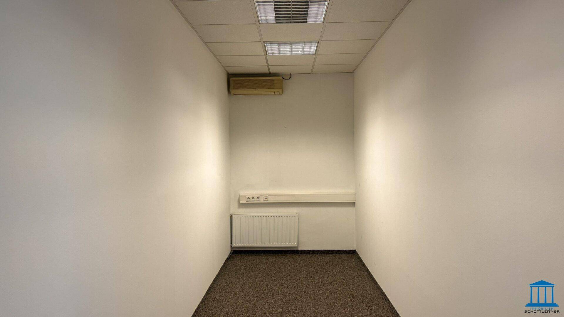 Kleiner Abstellraum mit Teppichboden, Heizkörper und Klimaanlage, ideal für technische Geräte.