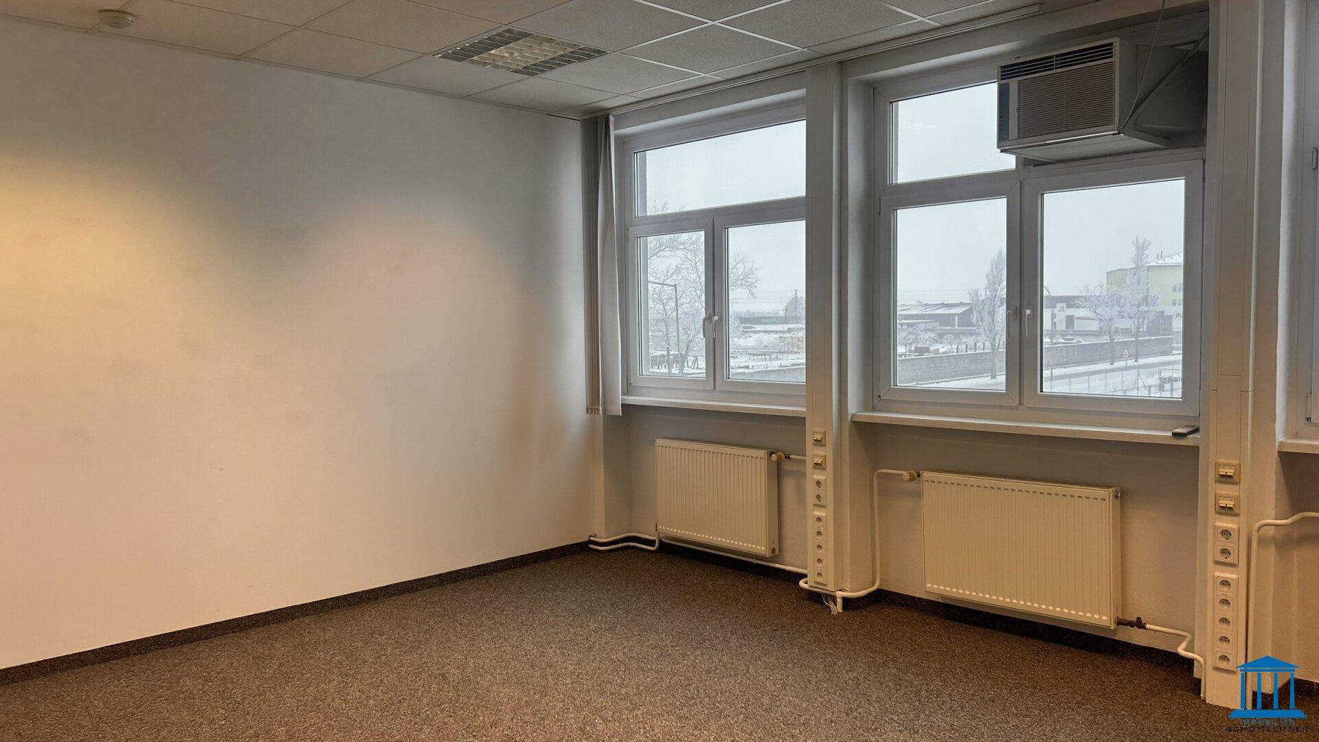 Büro mit Teppichboden, großen Fenstern und Klimaanlage, bietet viel Tageslicht und Komfort.