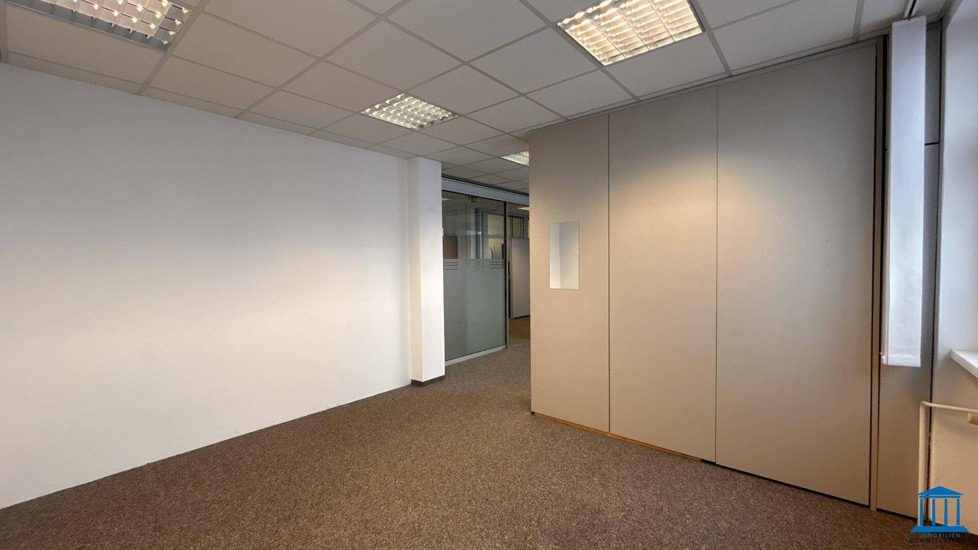 Büro mit Teppichboden, weißen Wänden und einer Trennwand, die den Raum strukturiert.