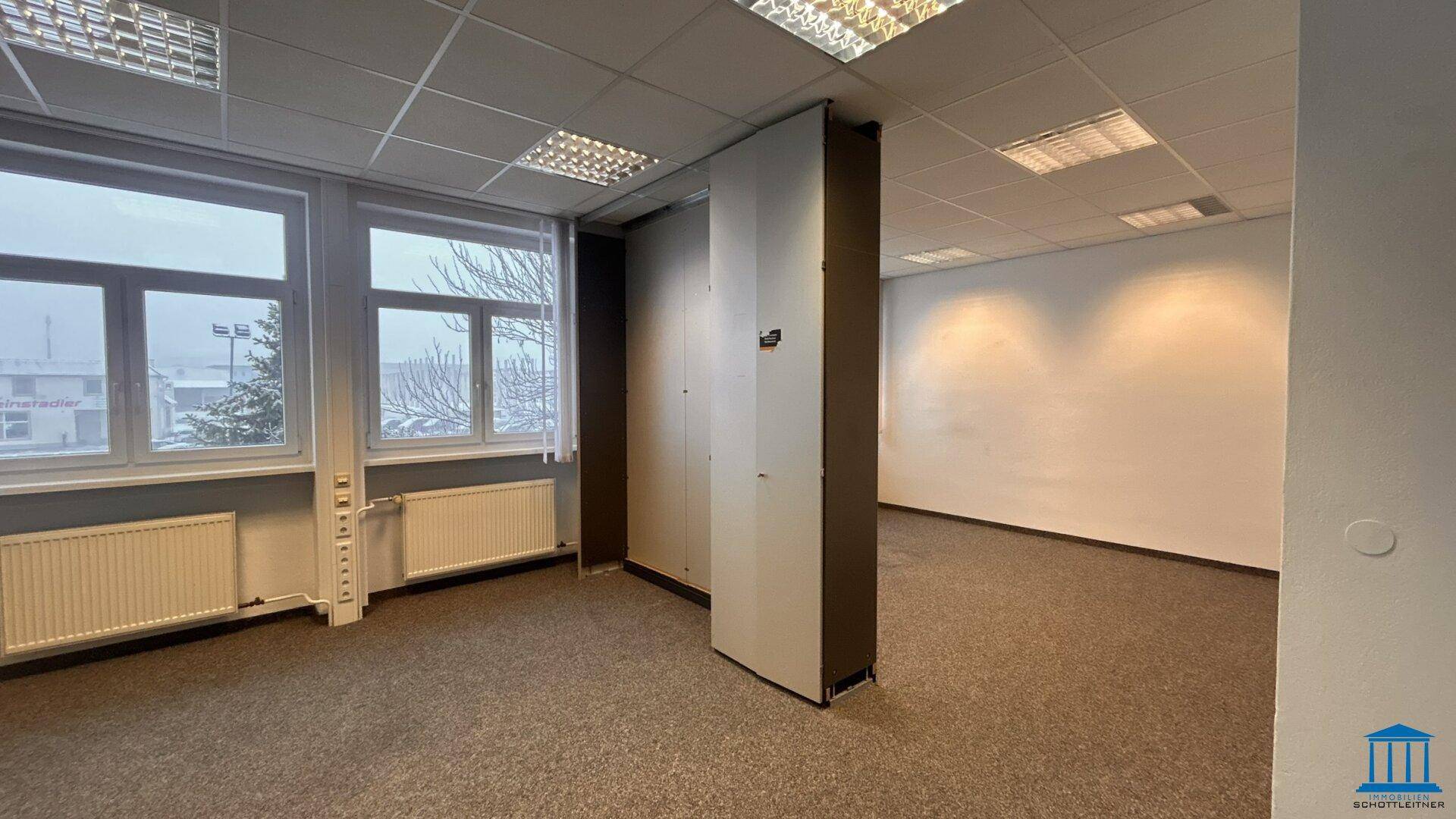 Geräumiges Büro mit Teppichboden, großen Fenstern und integrierten Schränken für Stauraum.