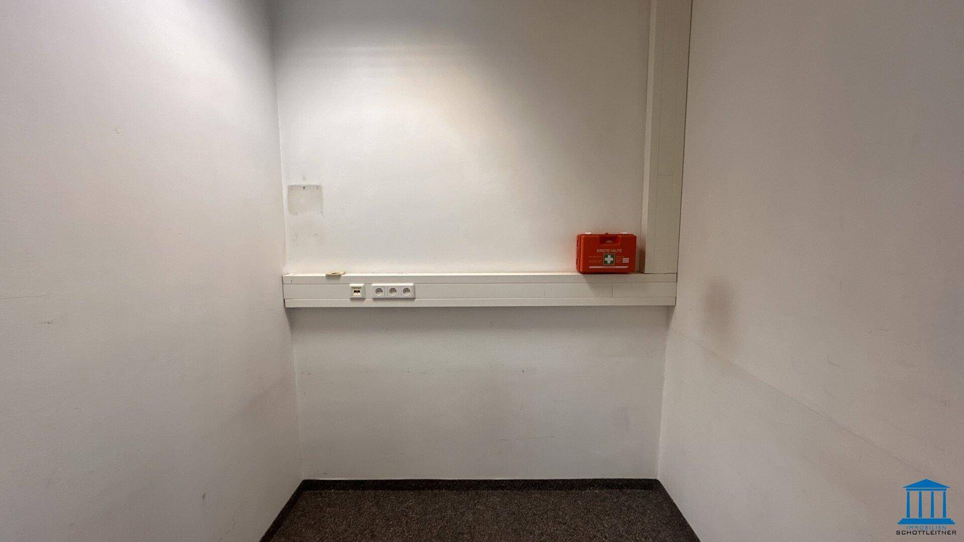 Kleiner Raum mit Teppichboden und Wandleiste mit Steckdosen, geeignet für Lagerung oder Technik.
