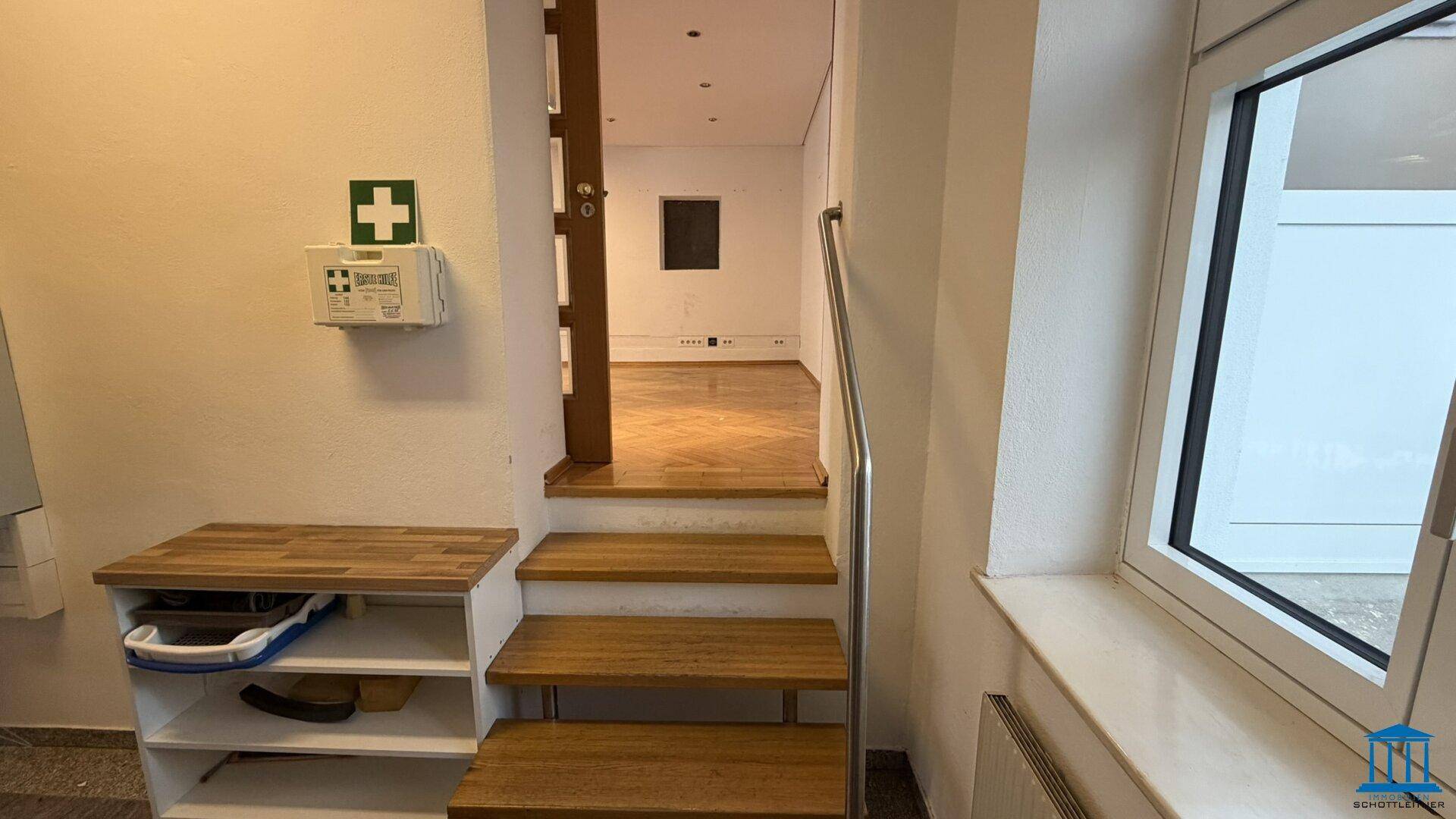 Treppenbereich mit Holzstufen, Metallgeländer und einem Erste-Hilfe-Kasten an der Wand.