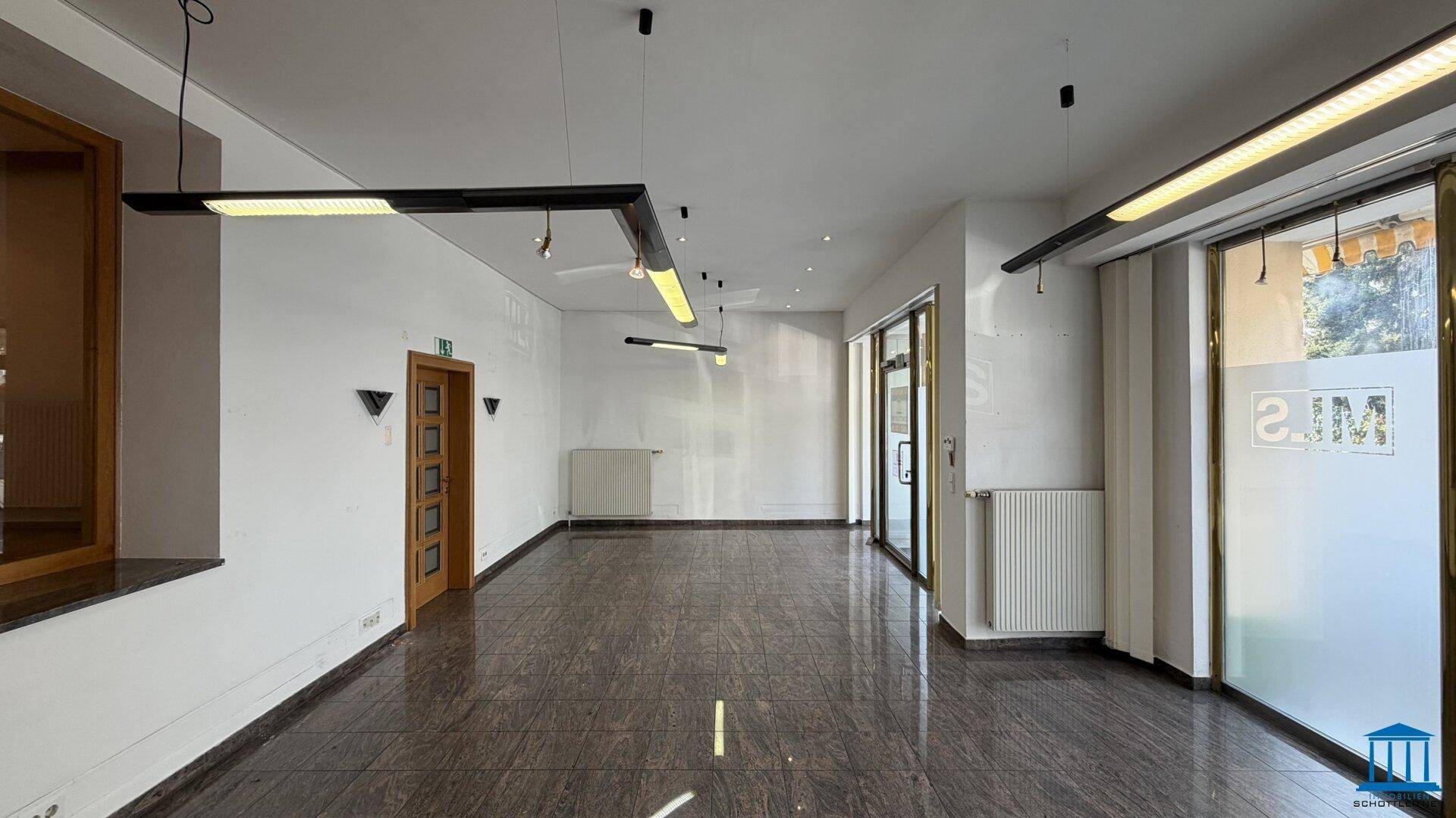 Weitläufiger Gewerberaum mit glänzendem Fliesenboden, weißen Wänden und modernen Deckenleuchten.