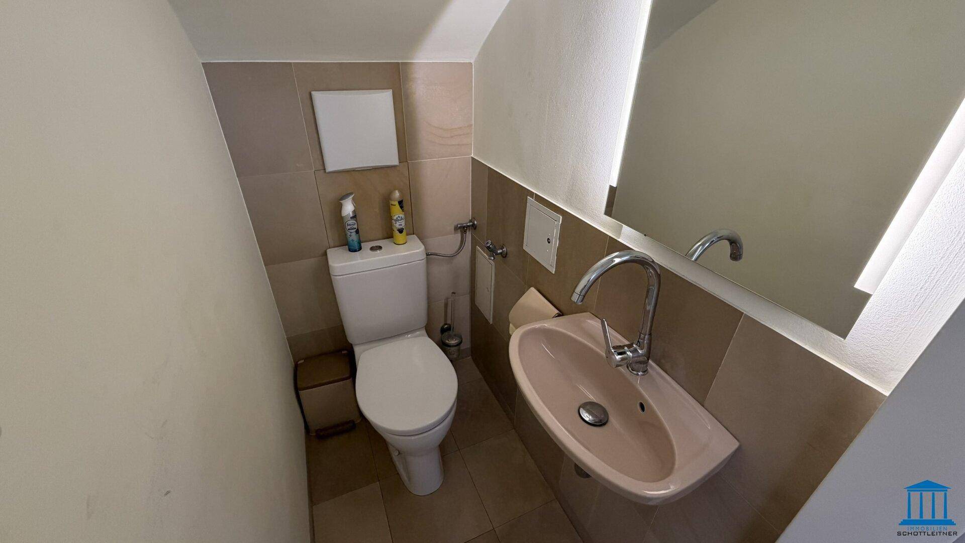 Kleines Badezimmer mit Toilette, Waschbecken und einem großen Spiegel, der den Raum optisch vergrößert.