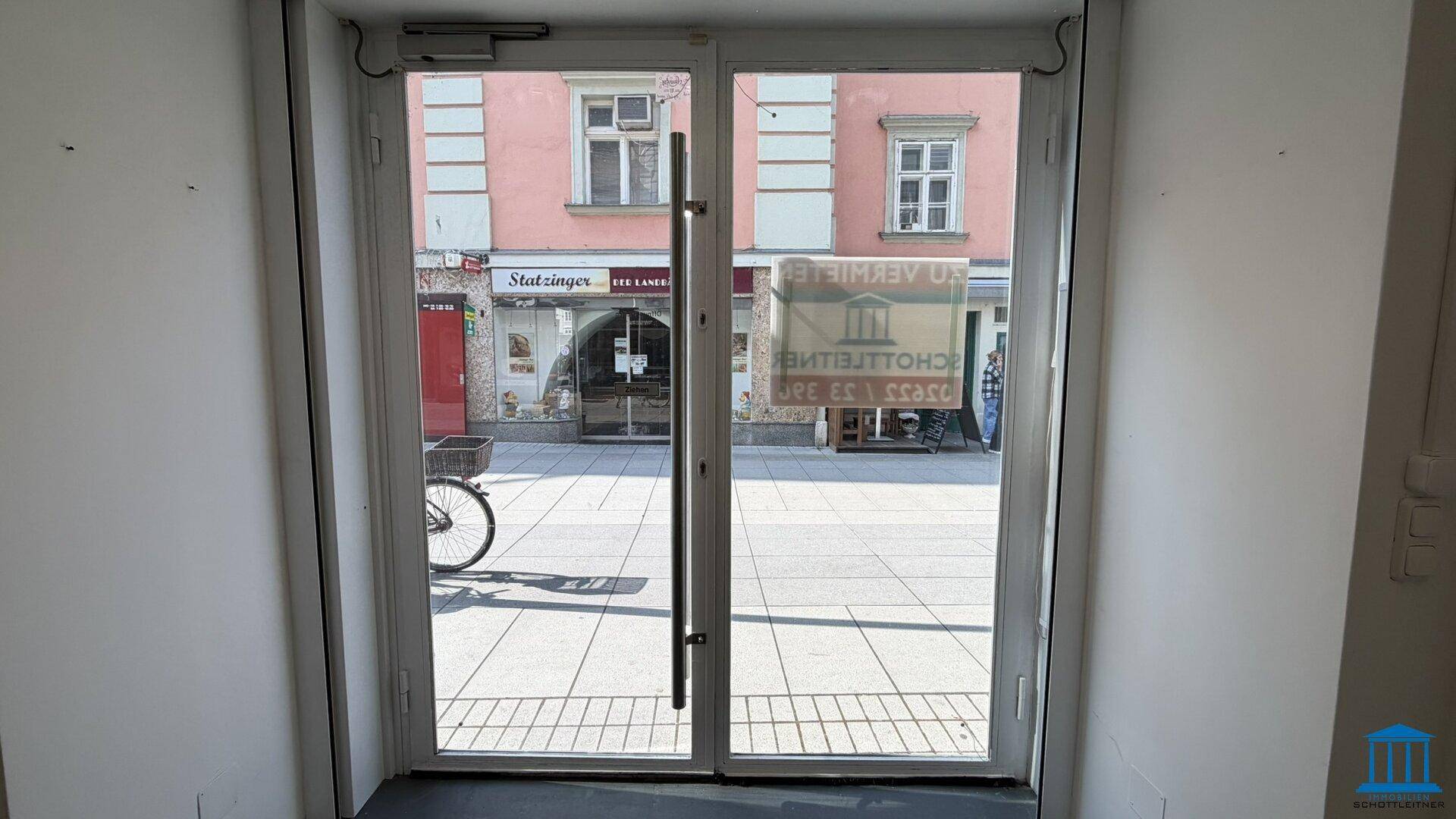 Blick von innen durch die Glastür auf die belebte Straße und gegenüberliegende Gebäude.