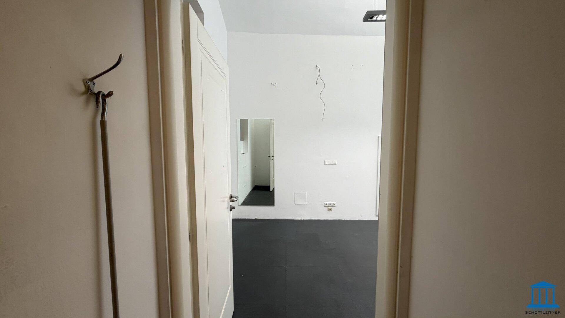Blick durch eine Tür in den Hauptgewerberaum mit dunklem Boden und weißen Wänden.