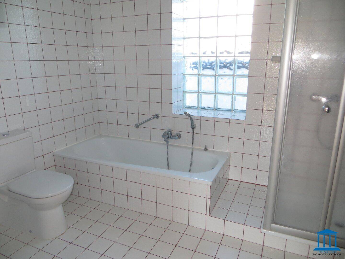Funktionales Badezimmer mit Badewanne, Dusche, WC und weißen Fliesen, ausgestattet mit Haltegriffen.