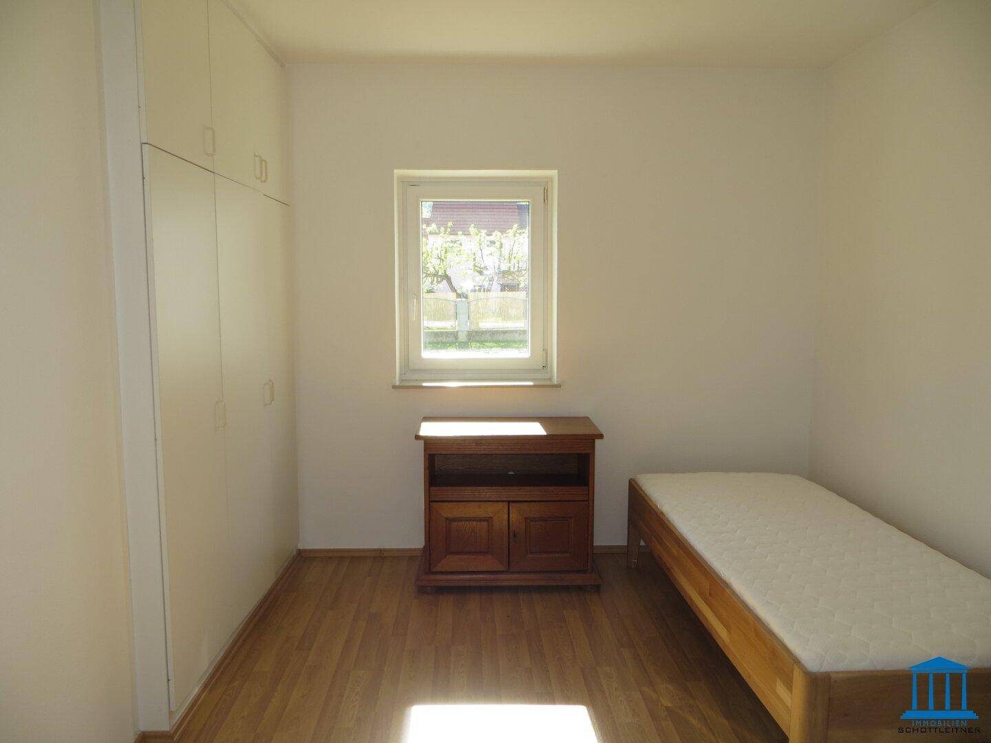 Schlafzimmer mit Einzelbett, praktischem Einbauschrank und Fenster mit Blick ins Grüne.