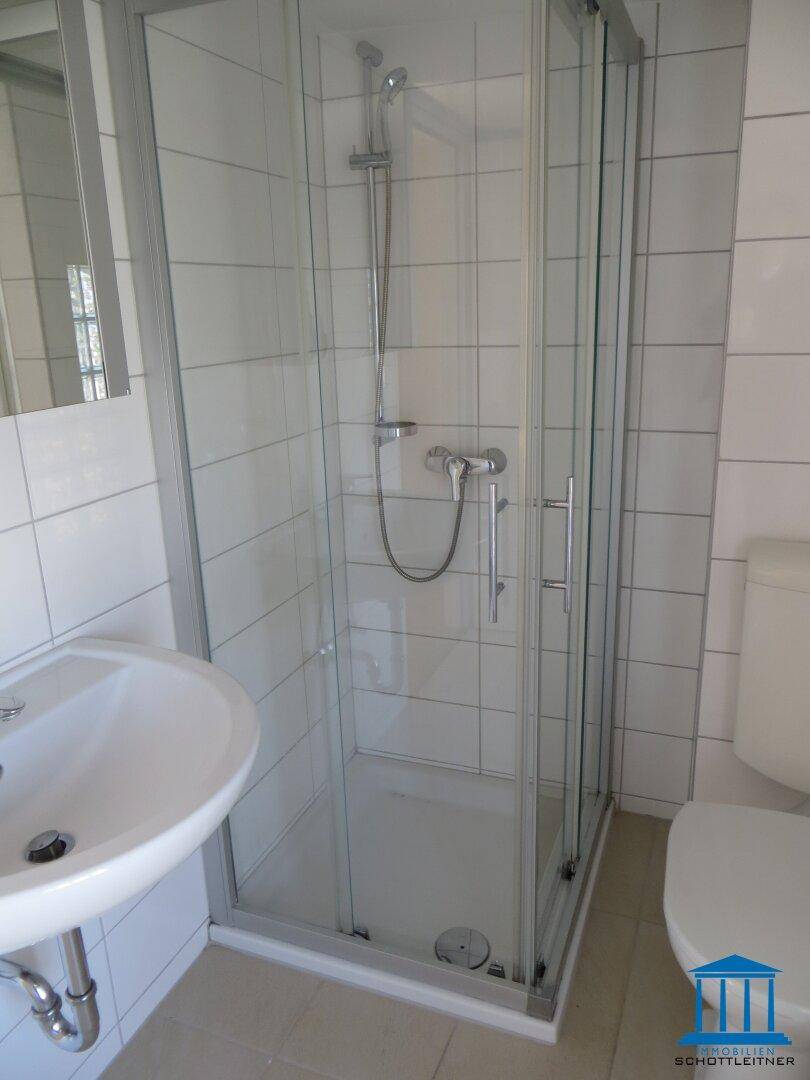 Helles Badezimmer mit Duschkabine, Einzelwaschbecken und WC, komplett gefliest.