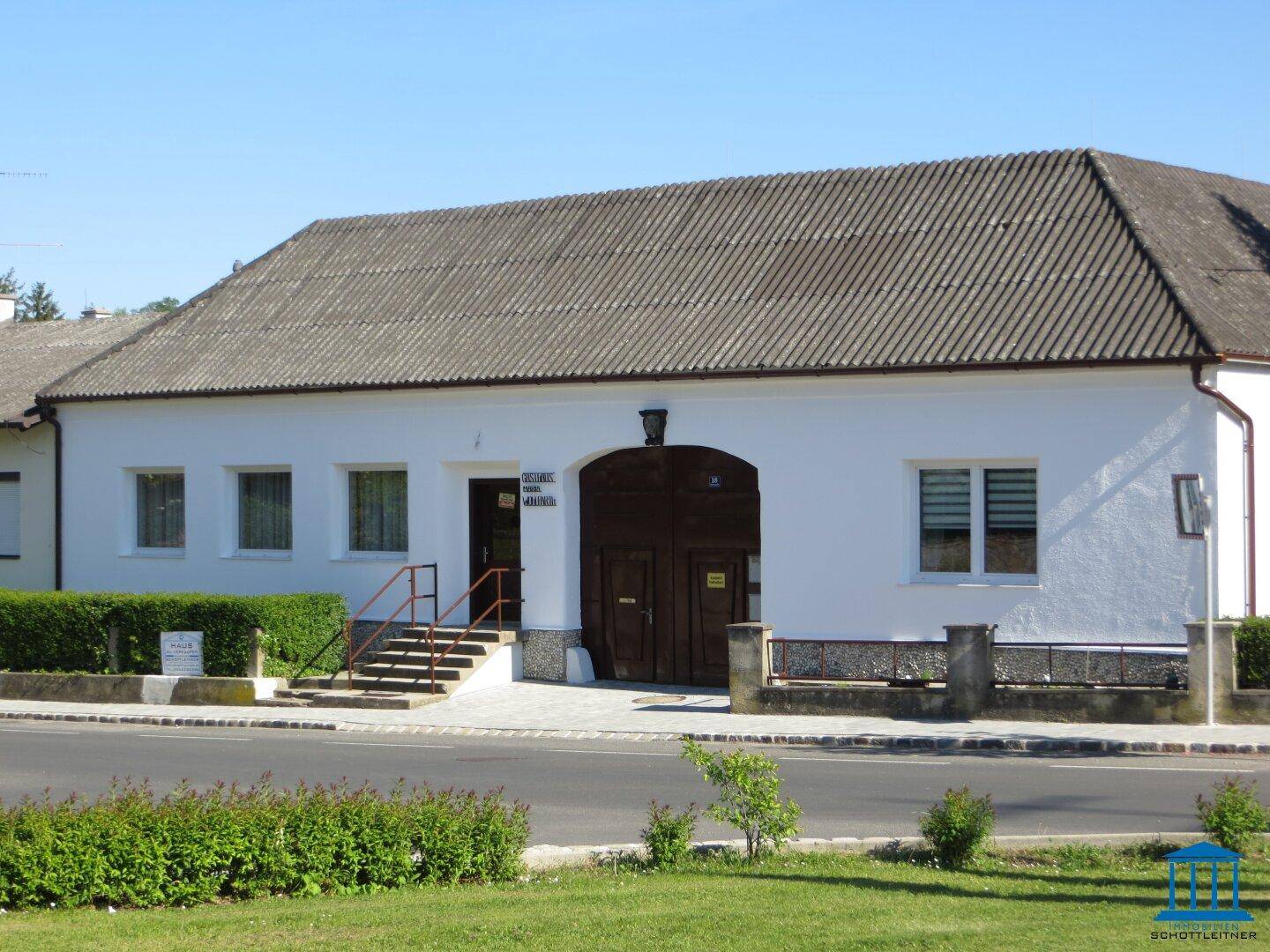 Historisches Nebengebäude mit weißer Fassade, großem Holztor und traditionellem Satteldach.