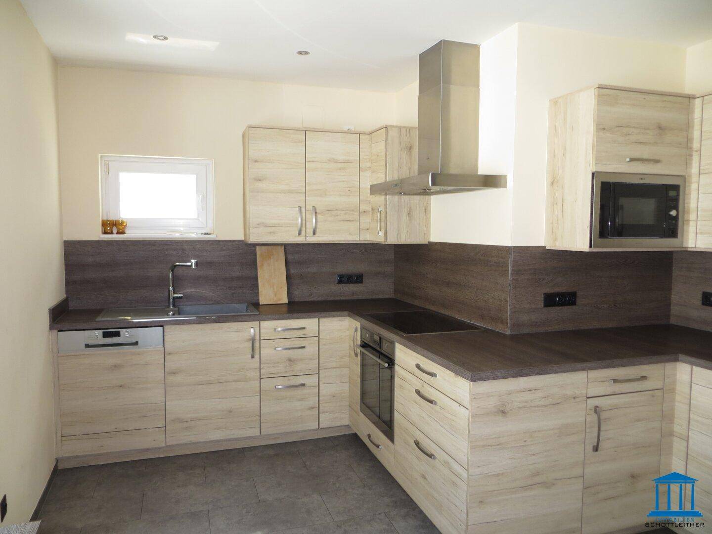 Moderne Einbauküche mit Holzoptik-Fronten, dunkler Arbeitsplatte und integrierten Geräten.