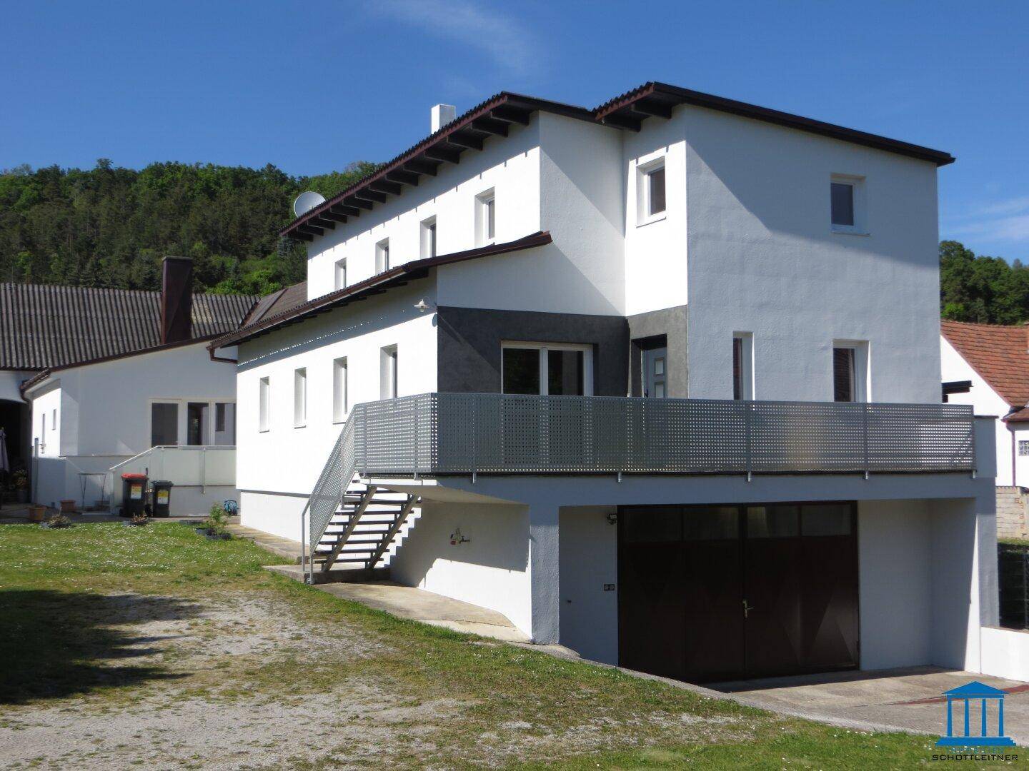 Seitenansicht des Wohnhauses mit Balkon, Außentreppe und integrierter Garage im Erdgeschoss.