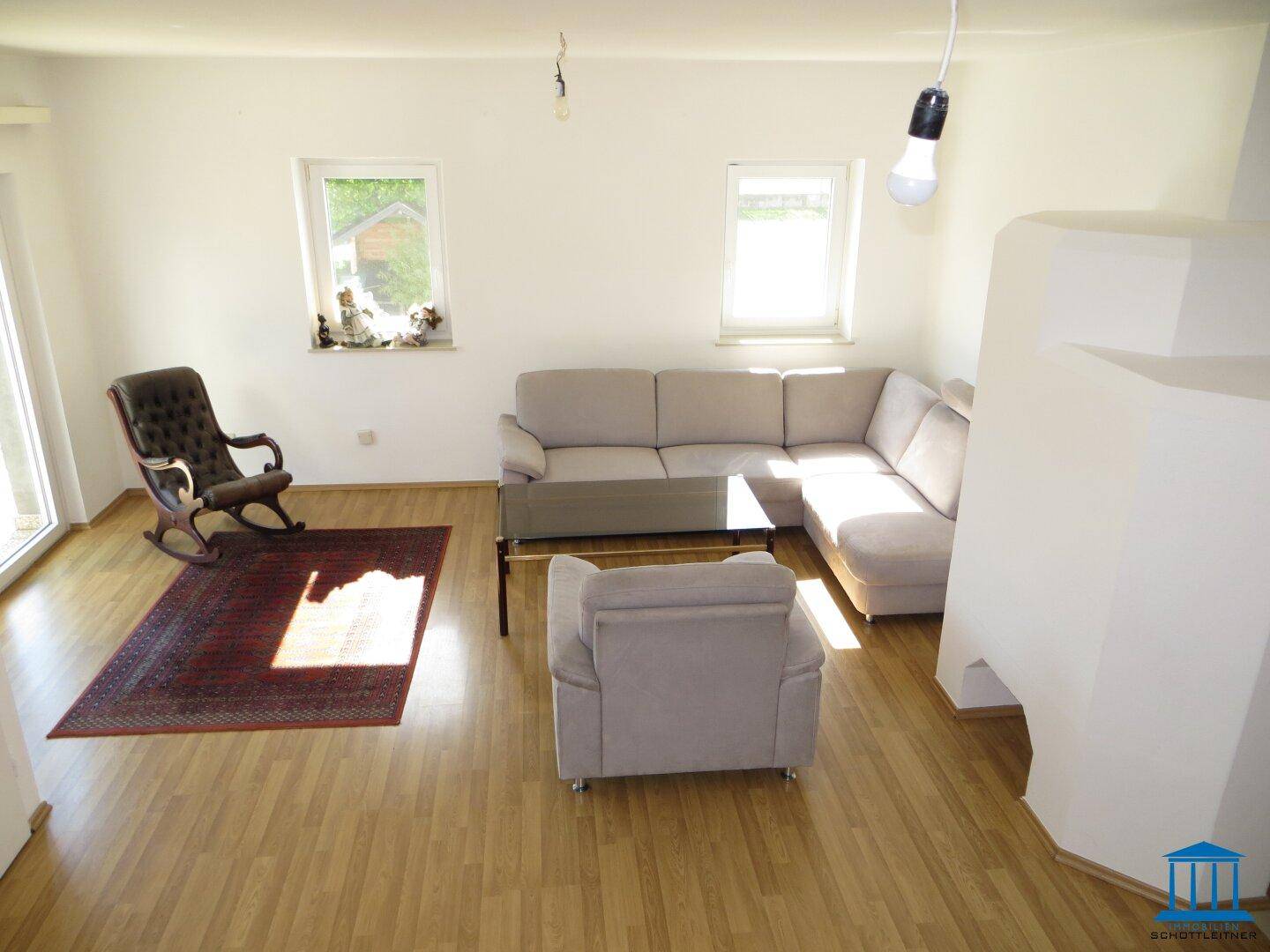 Geräumiges Wohnzimmer mit hellem Holzboden, gemütlicher Sitzecke und traditionellem Kachelofen.