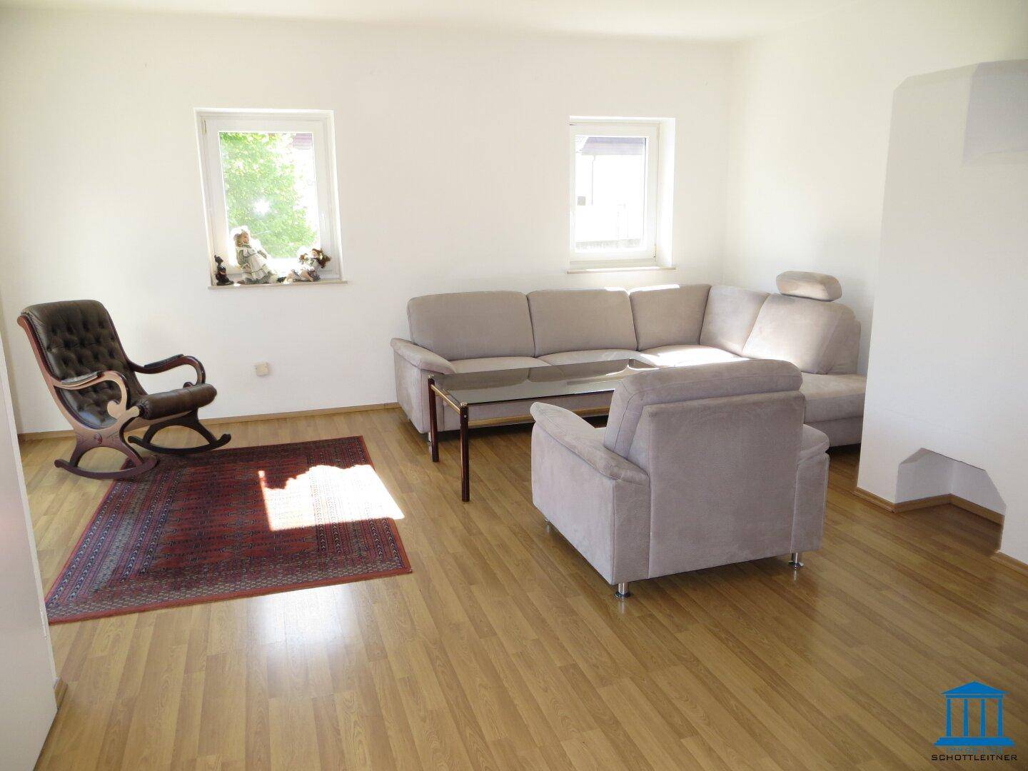Helles Wohnzimmer mit Parkettboden, beiger Couch und zwei Fenstern für viel Tageslicht.