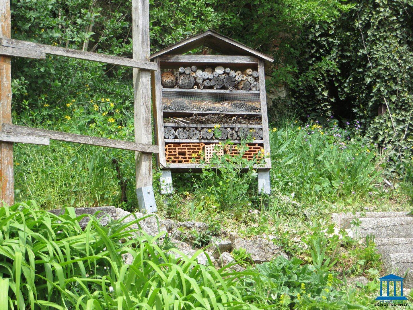 Detailansicht eines Insektenhotels in einem naturnahen Gartenbereich mit viel Grün.