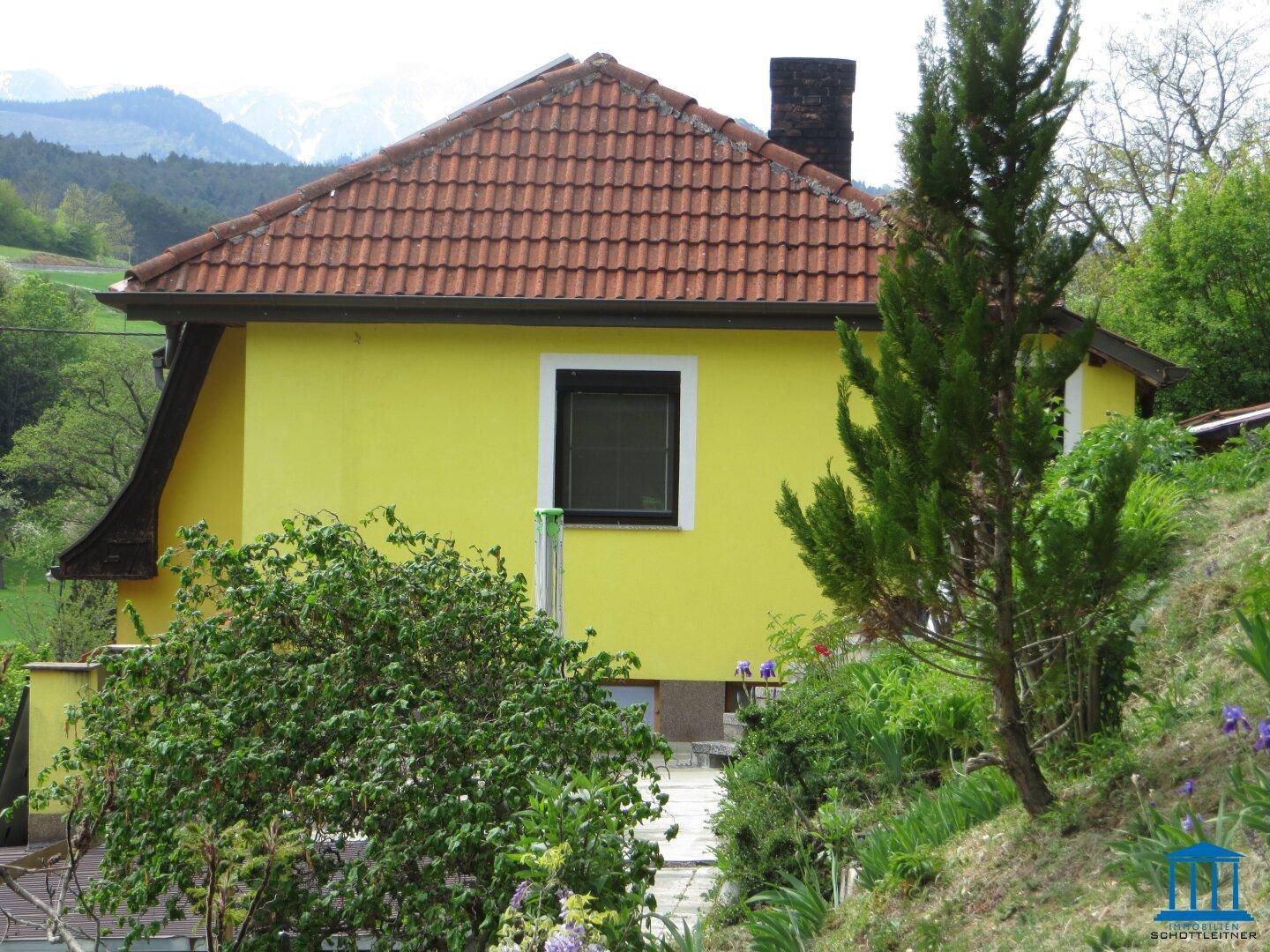 Rückseite des gelben Hauses mit rotem Dach und weitem Blick auf die Berge.