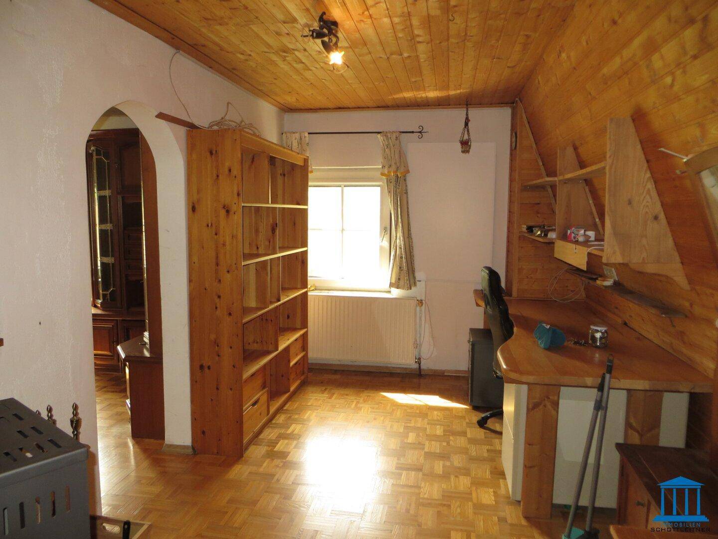 Zimmer mit Holzvertäfelung an Decke und Wänden, Holzboden und Schreibtisch.