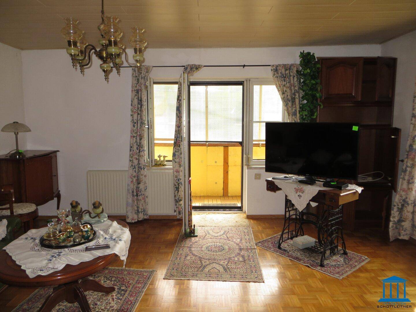 Gemütliches Wohnzimmer mit Parkettboden, Kronleuchter und Zugang zu einem kleinen Balkon.