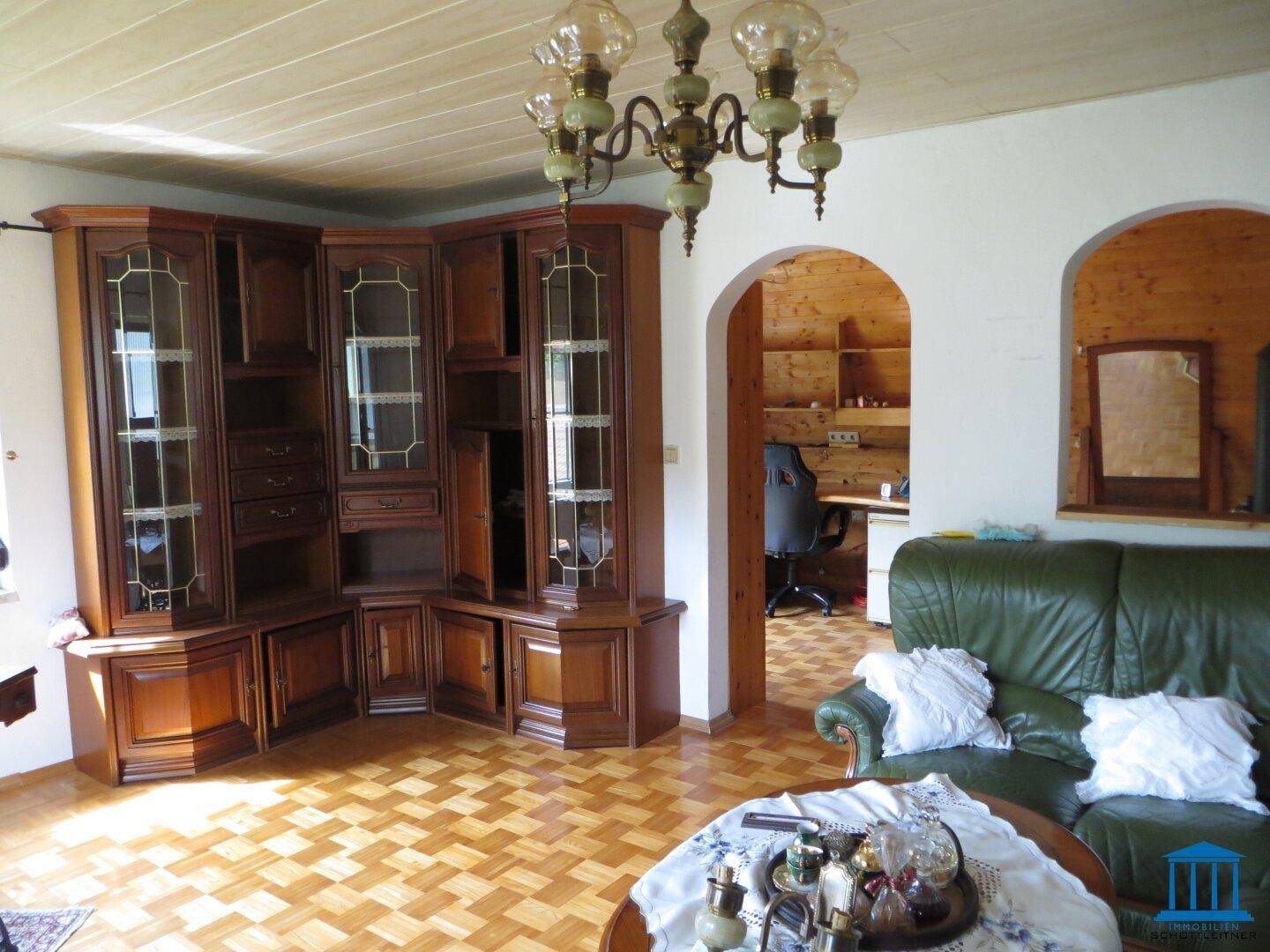 Wohnzimmer mit großem Eckschrank aus Holz, grüner Ledercouch und Parkettboden.