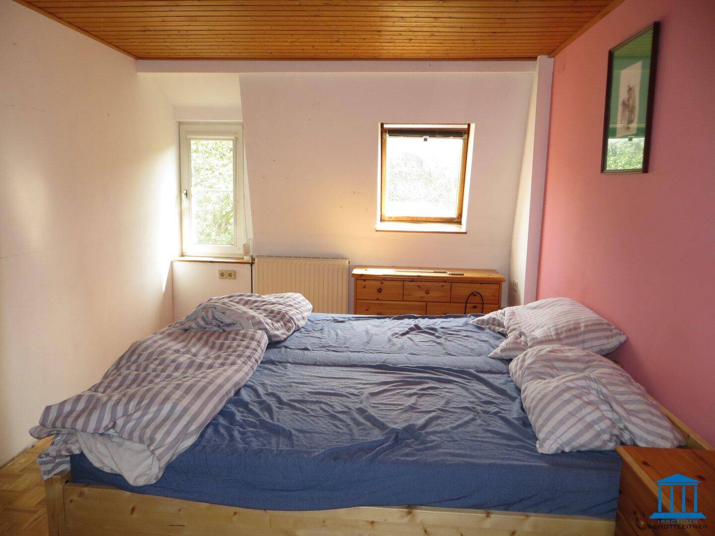 Schlafzimmer mit Holzbett, rosa Wandakzenten und zwei Fenstern für natürliches Licht.