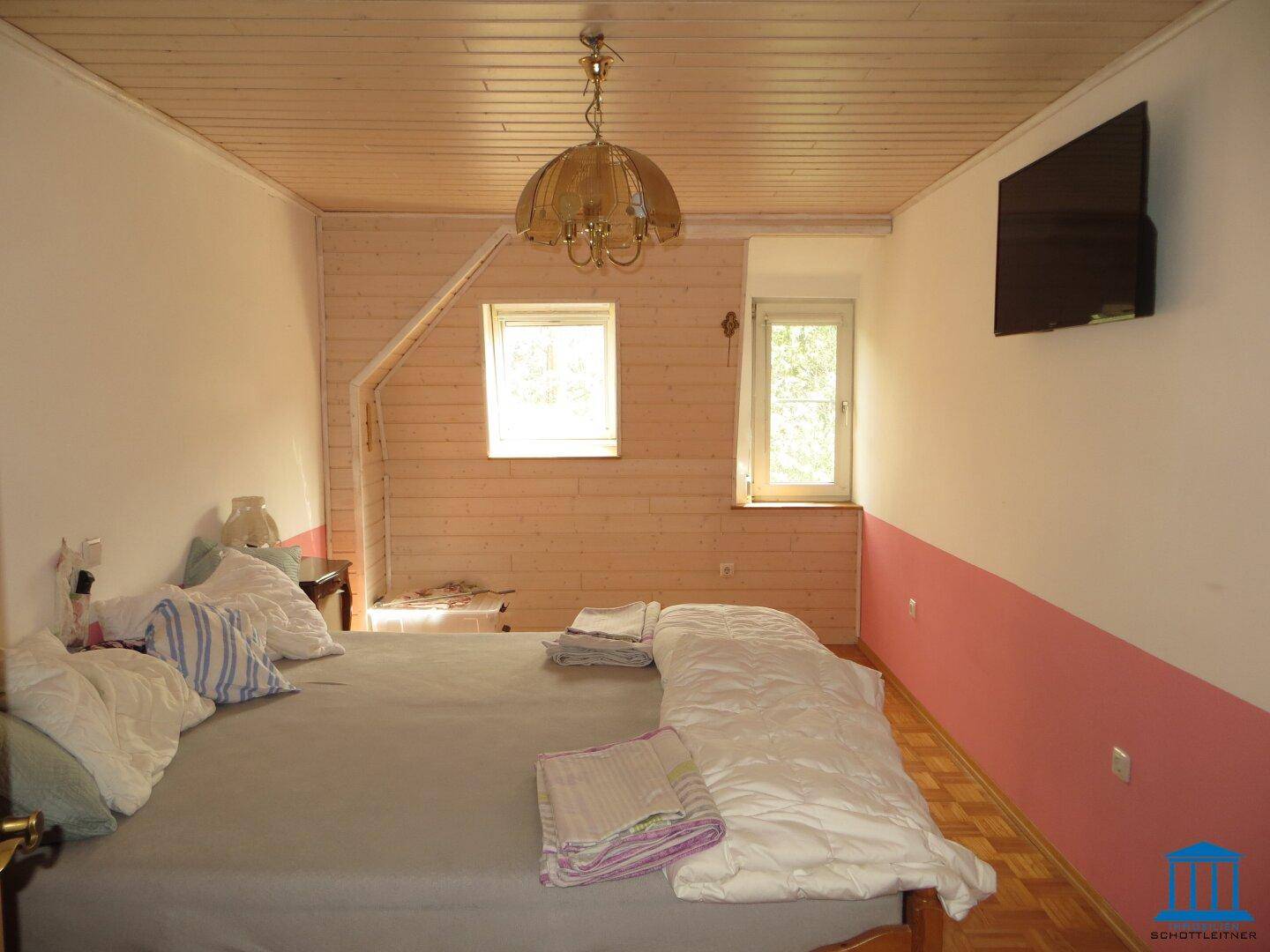 Schlafzimmer mit Holzboden, Holzdecke und rosa Wandakzenten, ausgestattet mit einem Fernseher.