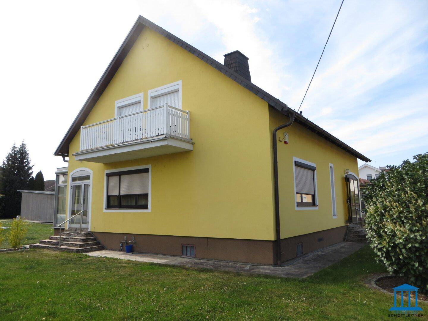 Rückseite des gelben Hauses mit Balkon und grünem Rasen.