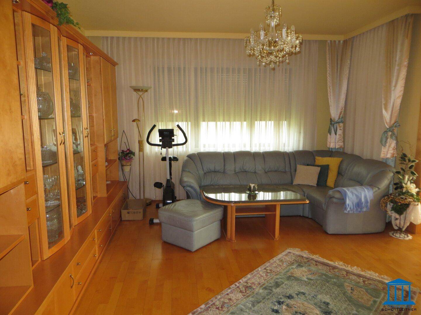 Wohnzimmer mit Parkettboden, Ecksofa und Kronleuchter.