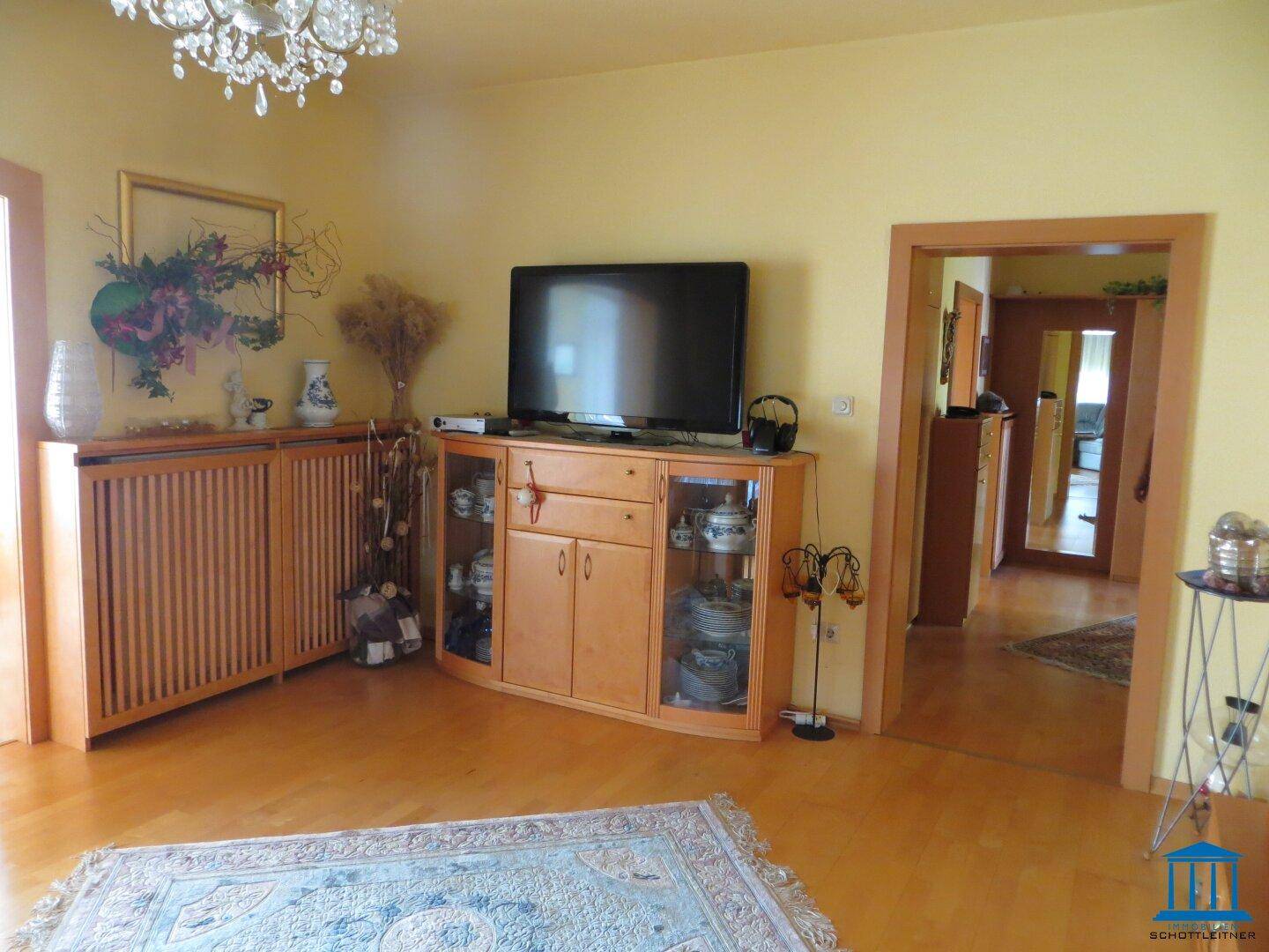 Wohnzimmer mit Holzboden, TV-Möbel und Blick in den Flur.